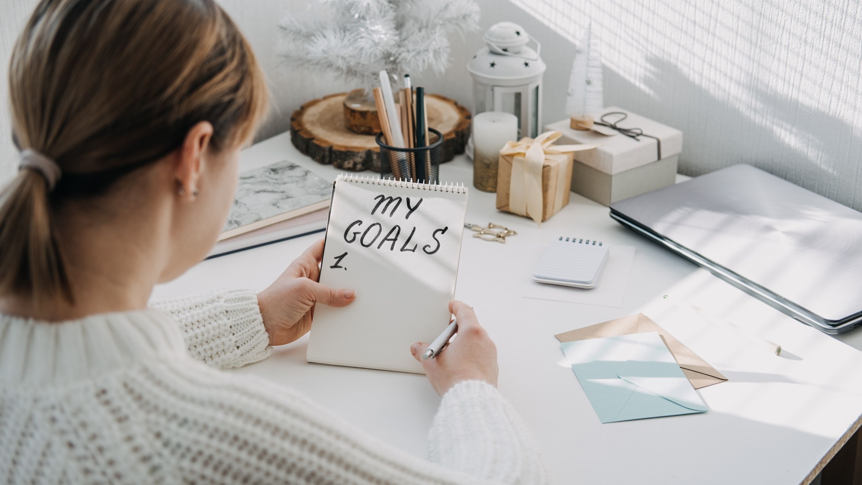 A woman writes 'My Goals' in large text on a small notepad.