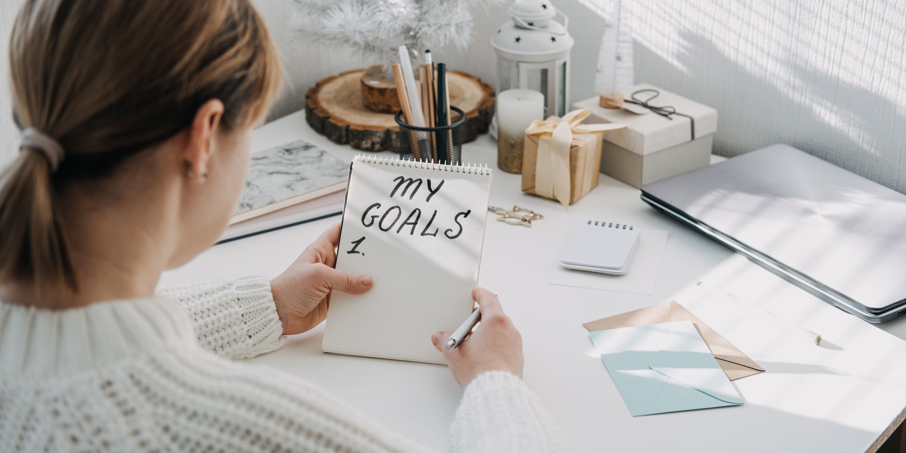 A woman writes 'My Goals' in large text on a small notepad.