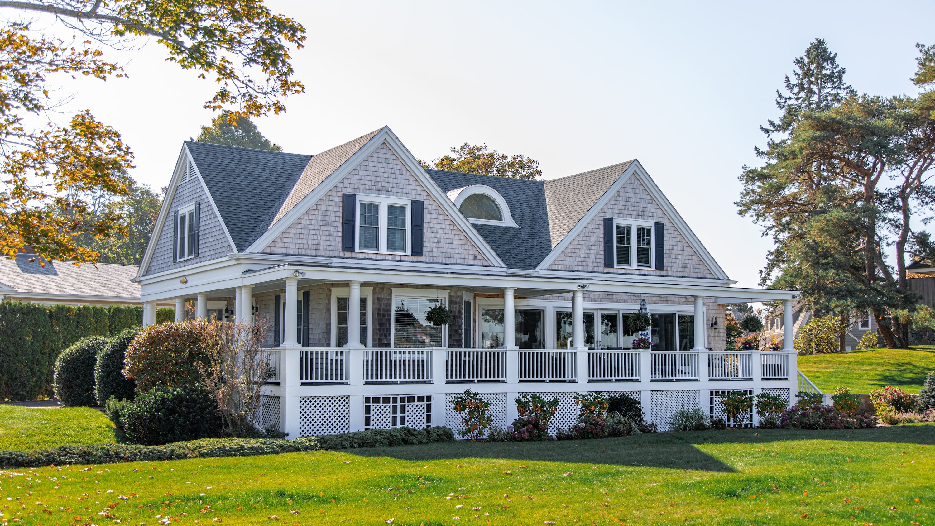 A grey house with a large porch overlooking a green yard.