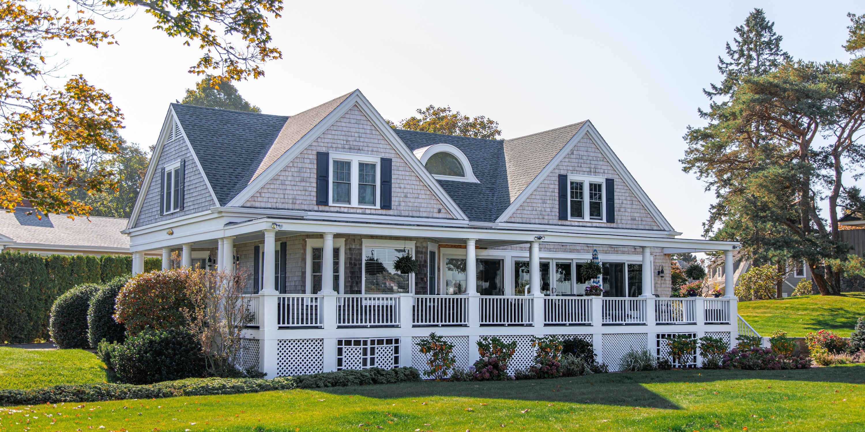 A grey house with a large porch overlooking a green yard.