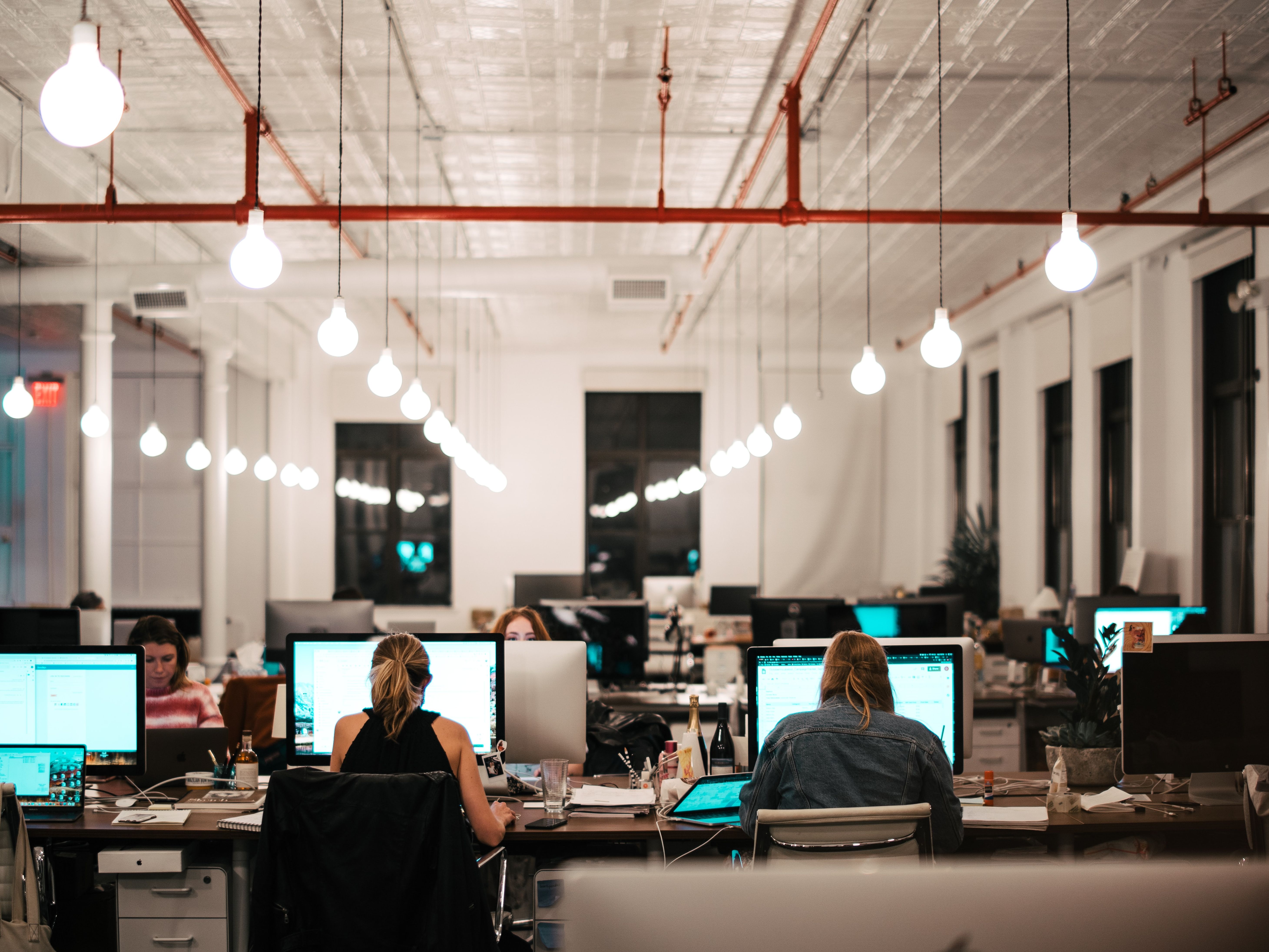 A group of young people conduct business on computers in a large warehouse space.
