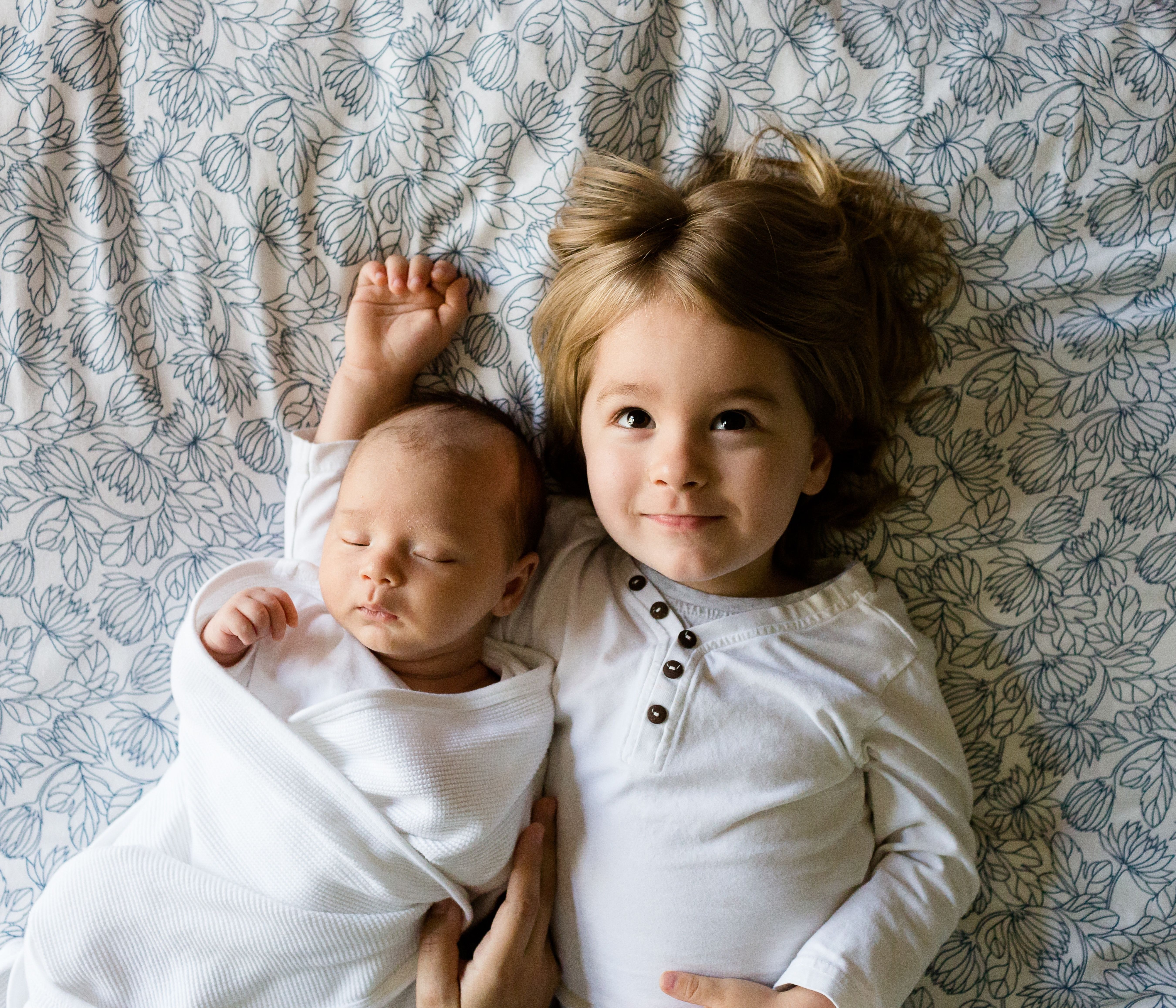 A young girl and a baby pose for a photo on a textured sheet backdrop.