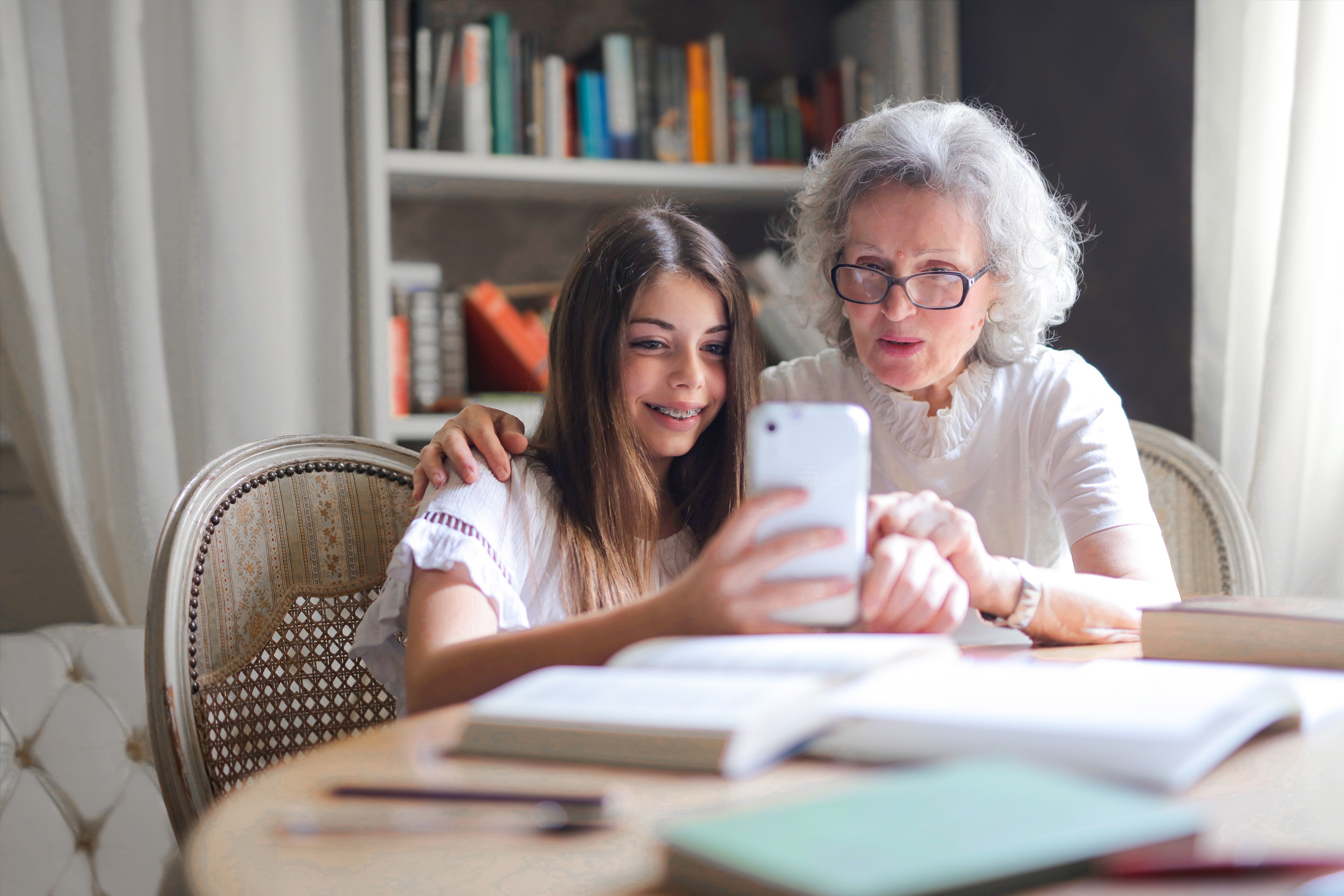 A young girl and her grandmother take a selfie together at a table covered in books.
