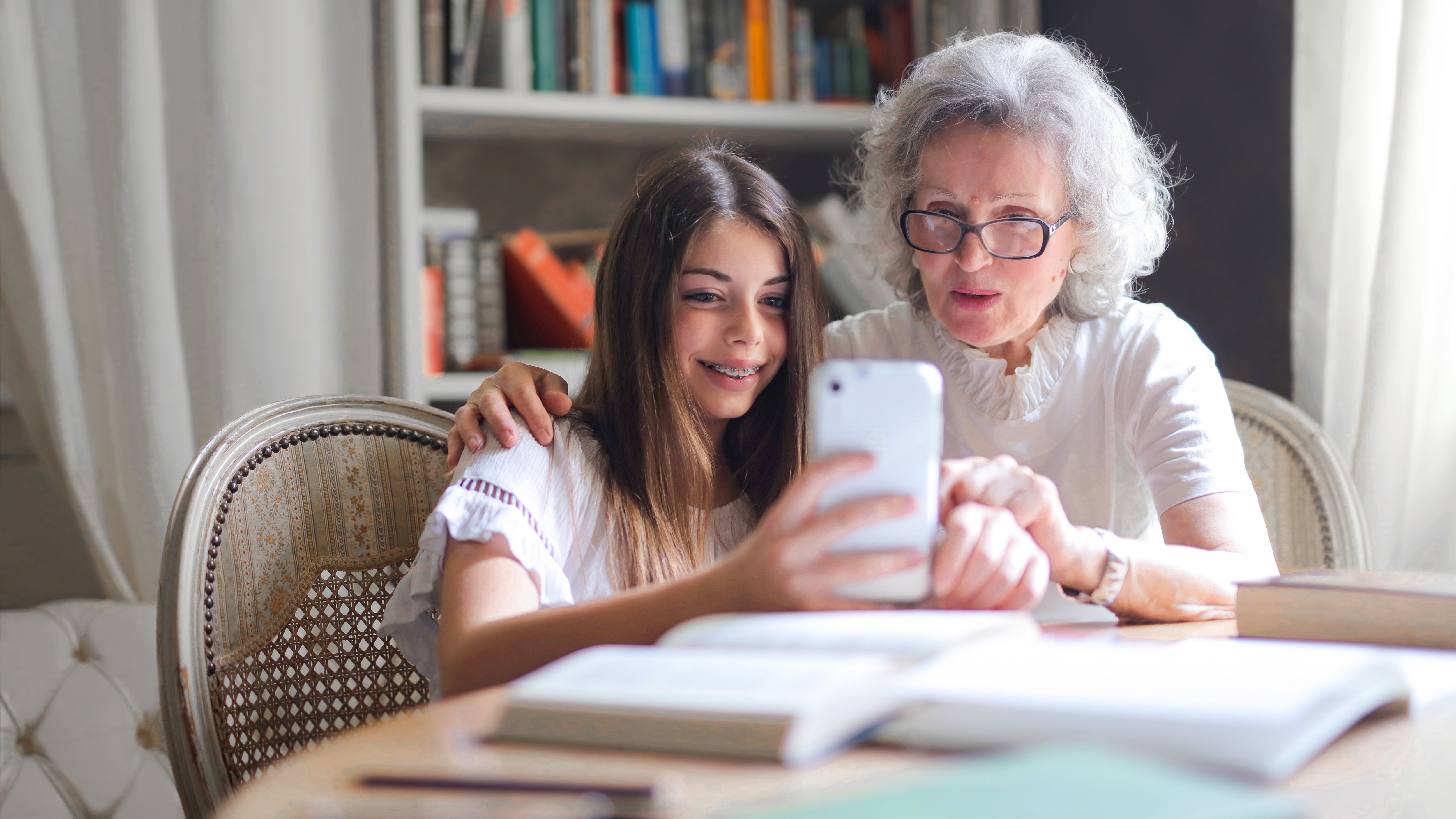 A young girl and her grandmother take a selfie together at a table covered in books.