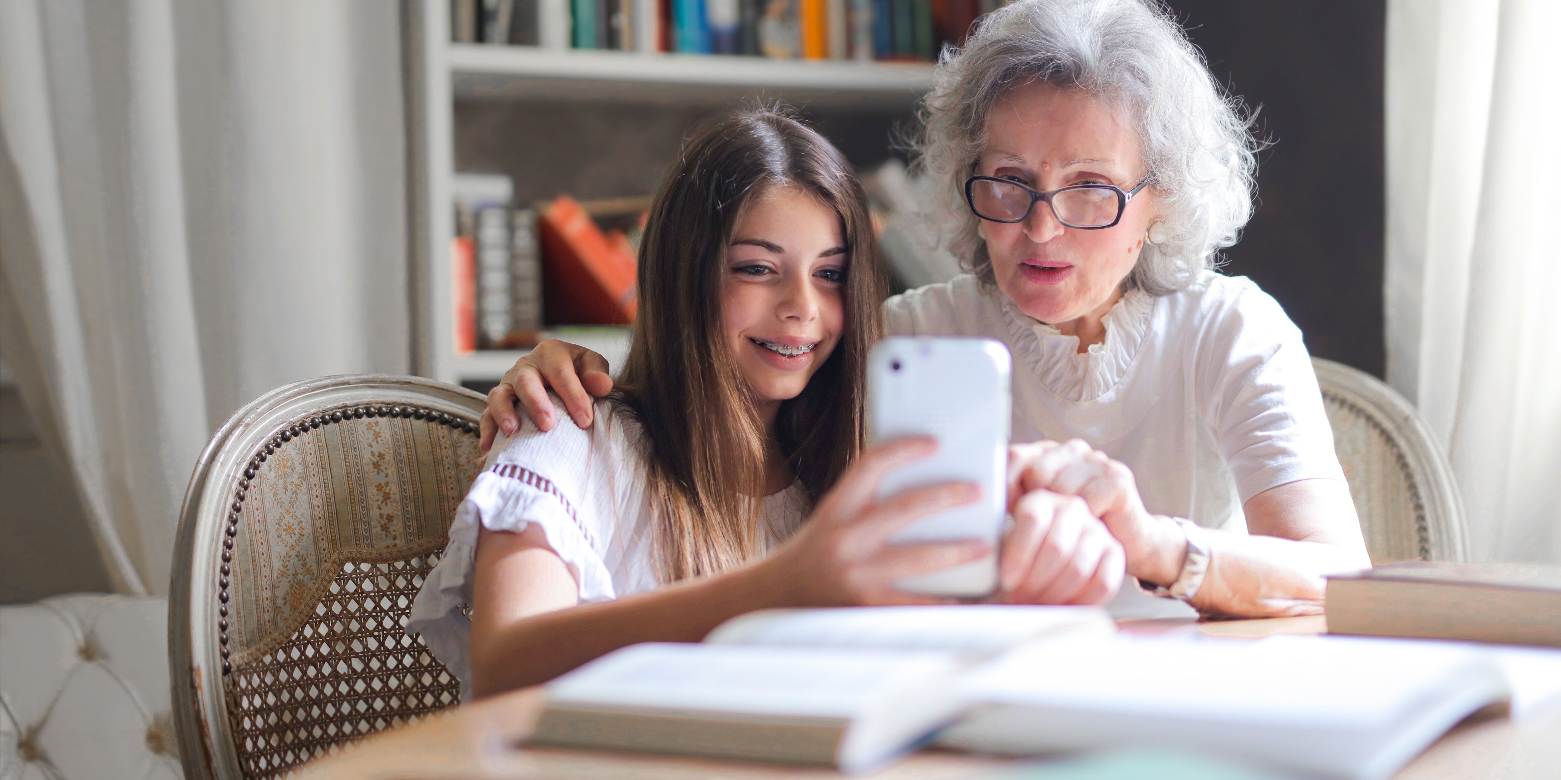 A young girl and her grandmother take a selfie together at a table covered in books.