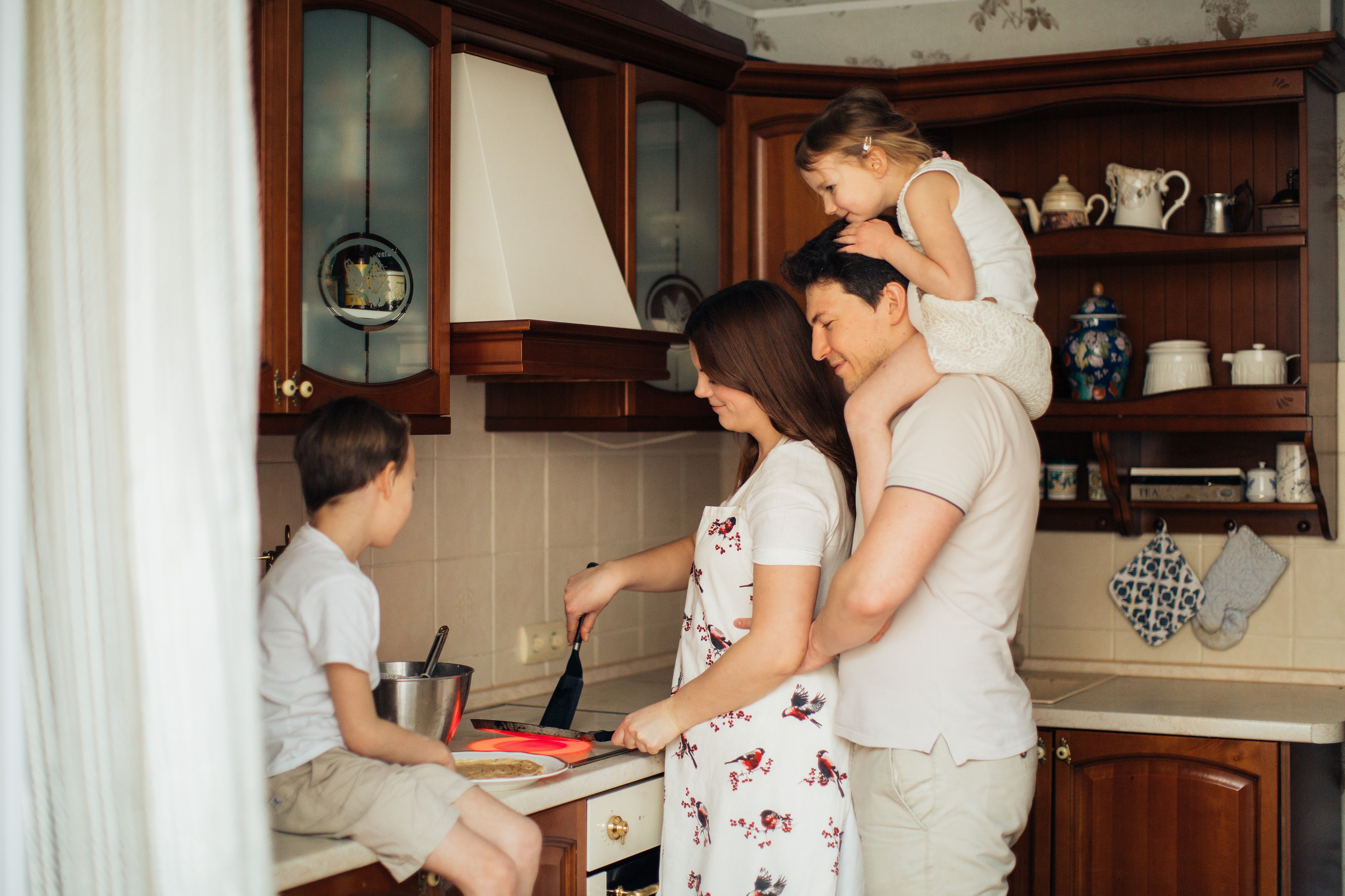 A family of four all gathers around the stove to flip a pancake.