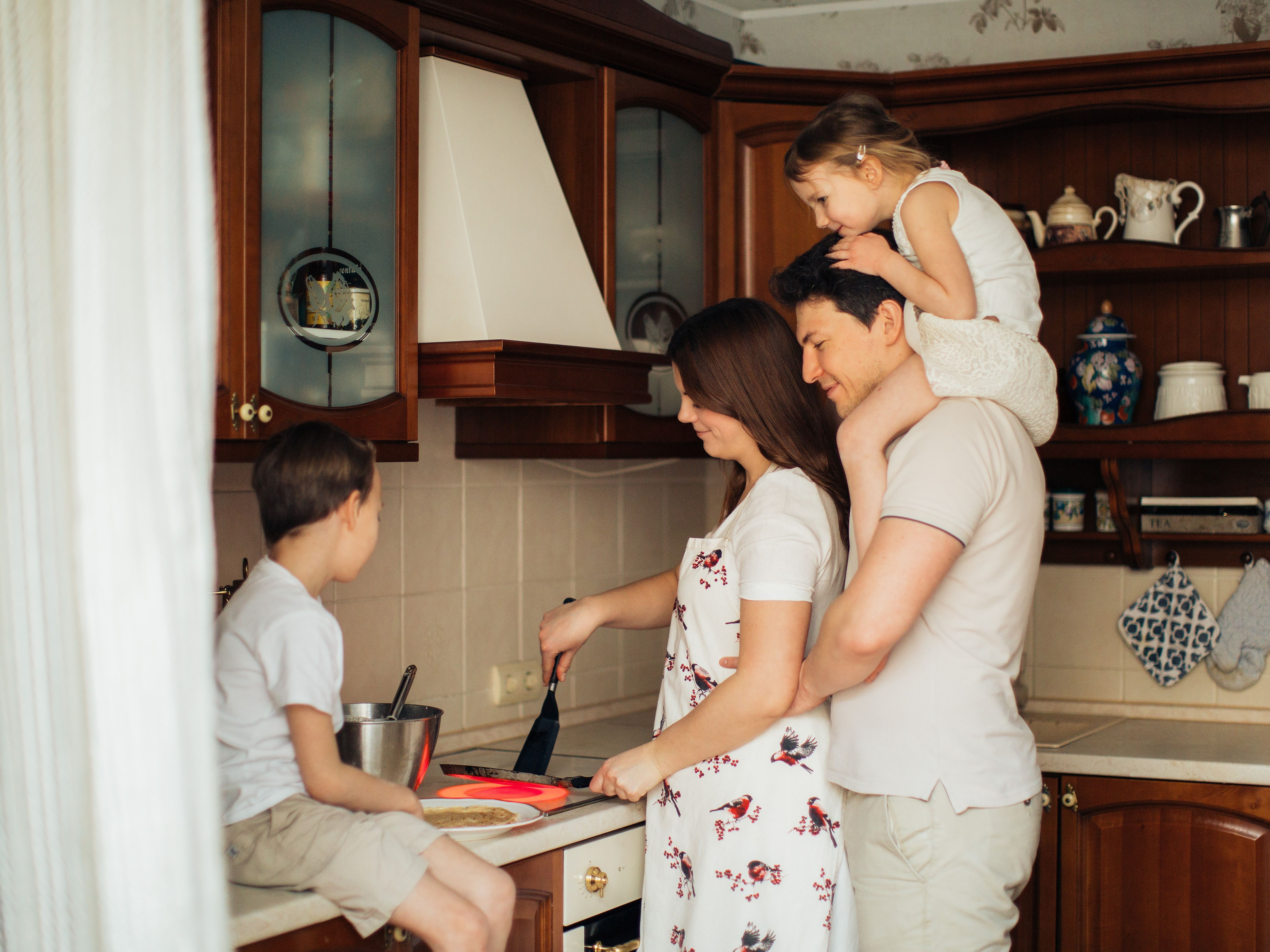 A family of four all gathers around the stove to flip a pancake.