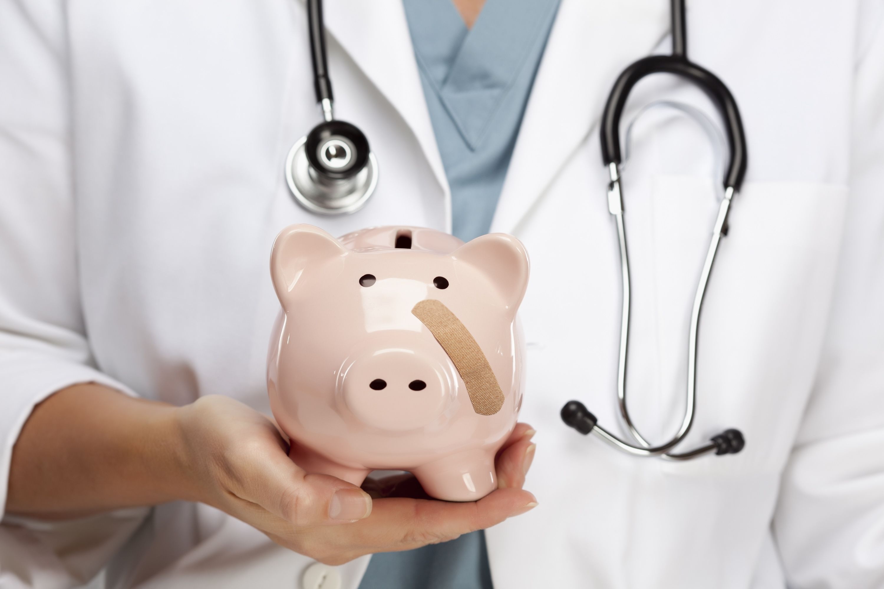 A doctor holds up a piggy bank with a band-aid on its cheek.