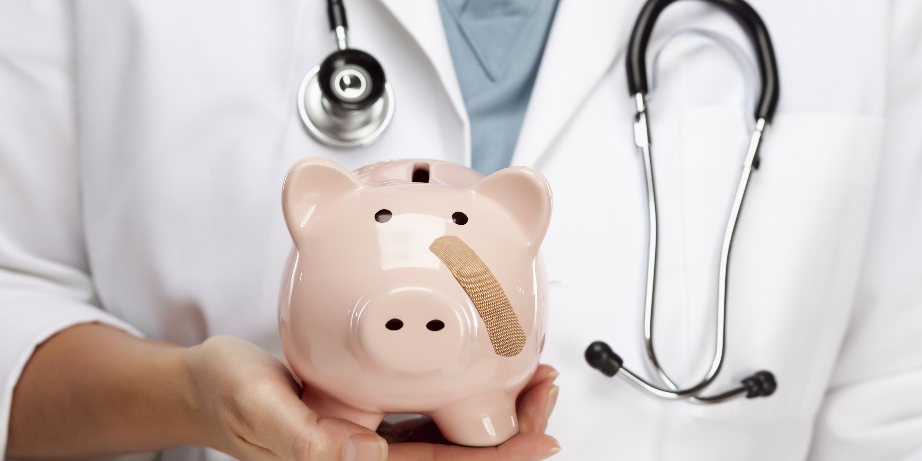 A doctor holds up a piggy bank with a band-aid on its cheek.