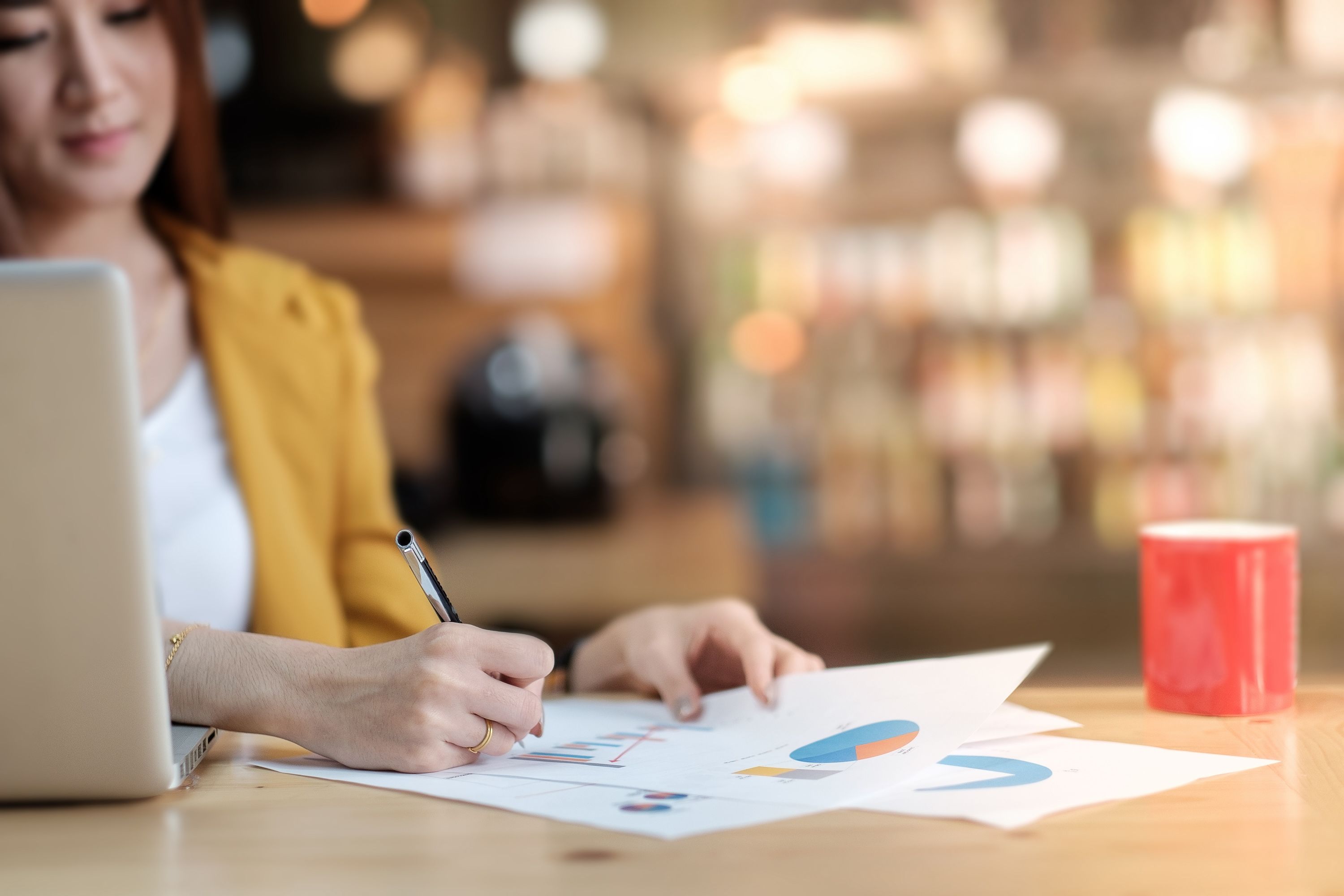 A woman writes on a bar graph next to a red coffee mug.