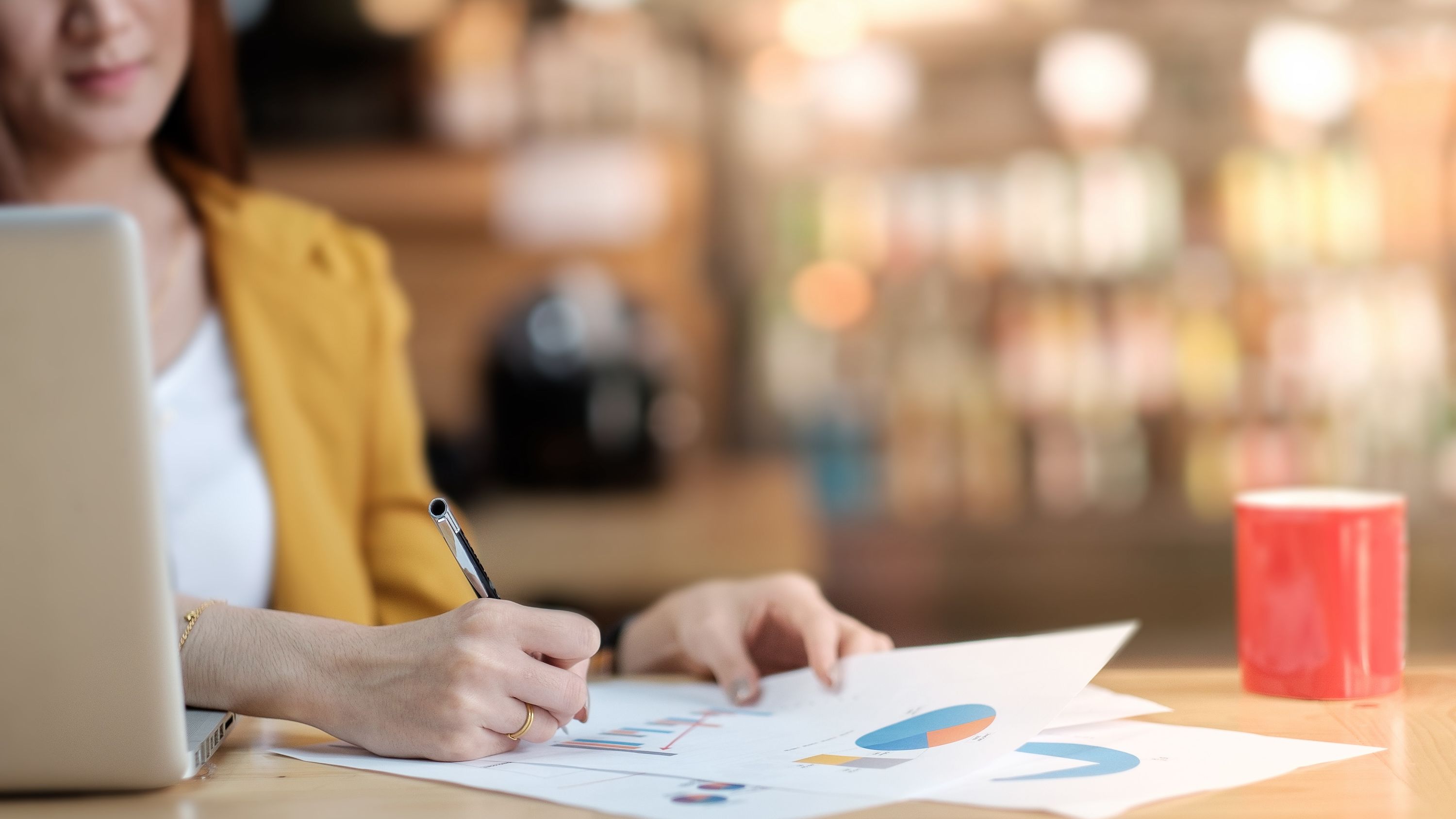 A woman writes on a bar graph next to a red coffee mug.