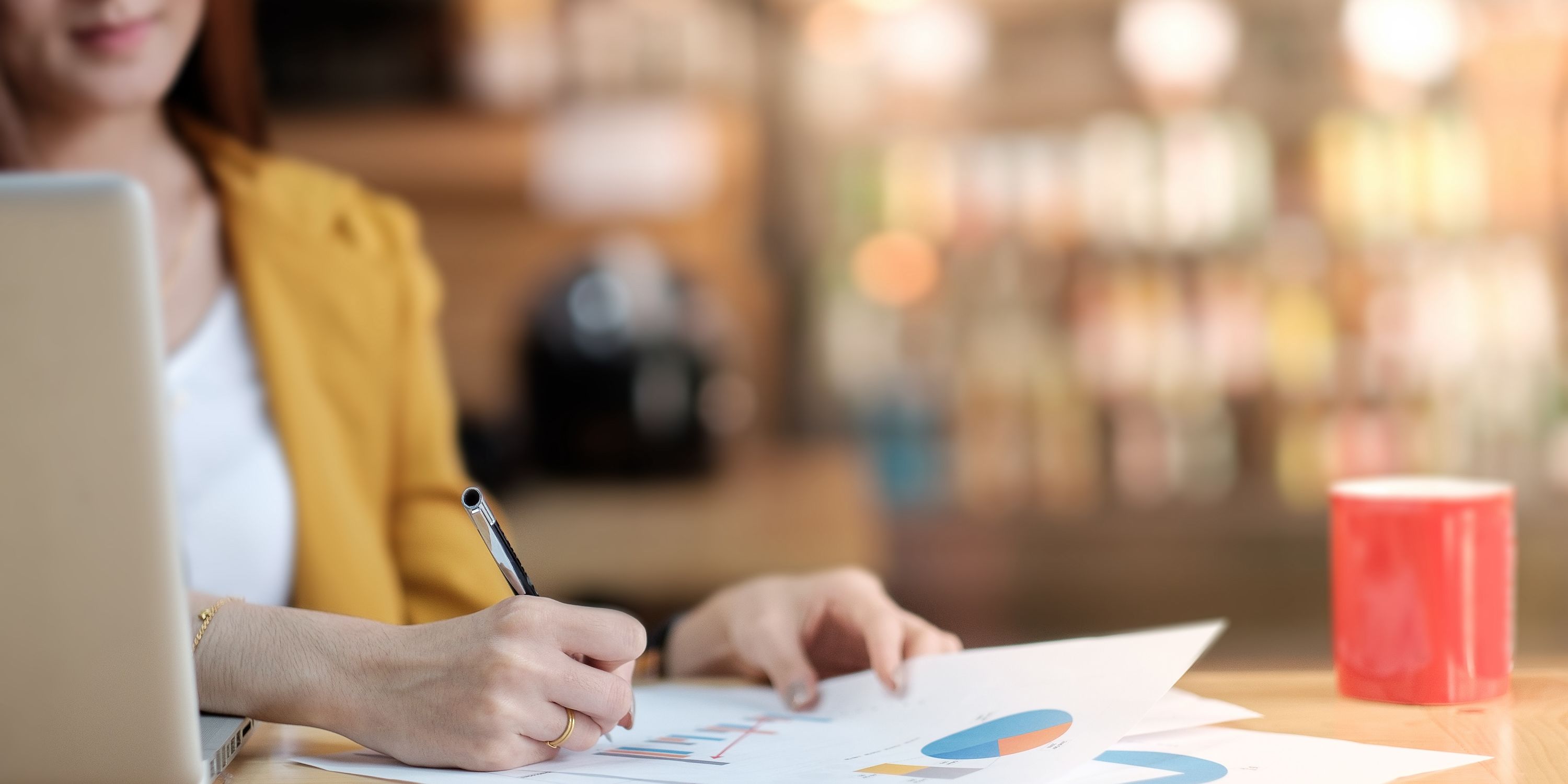 A woman writes on a bar graph next to a red coffee mug.