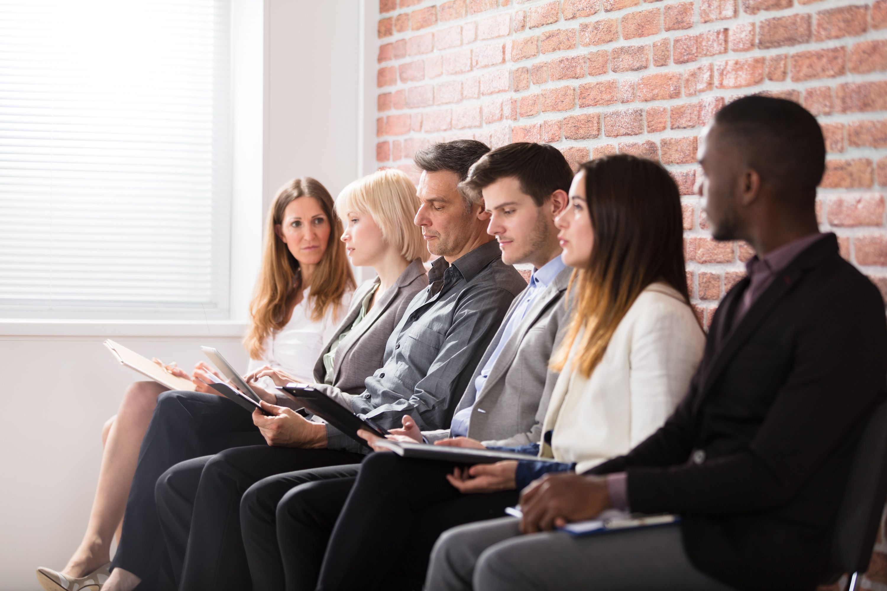 A group of interviewees line up against a brick wall.