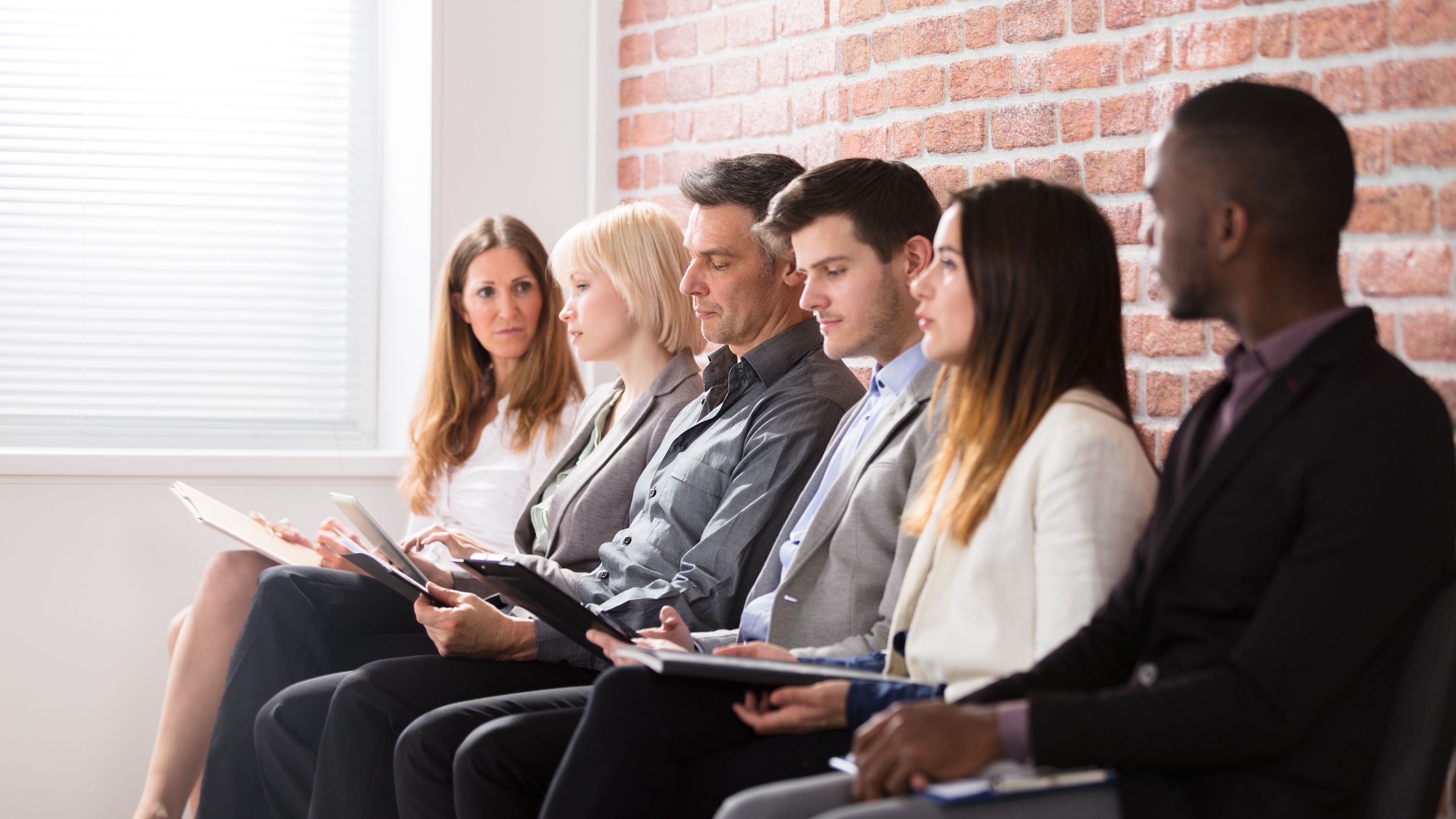 A group of interviewees line up against a brick wall.