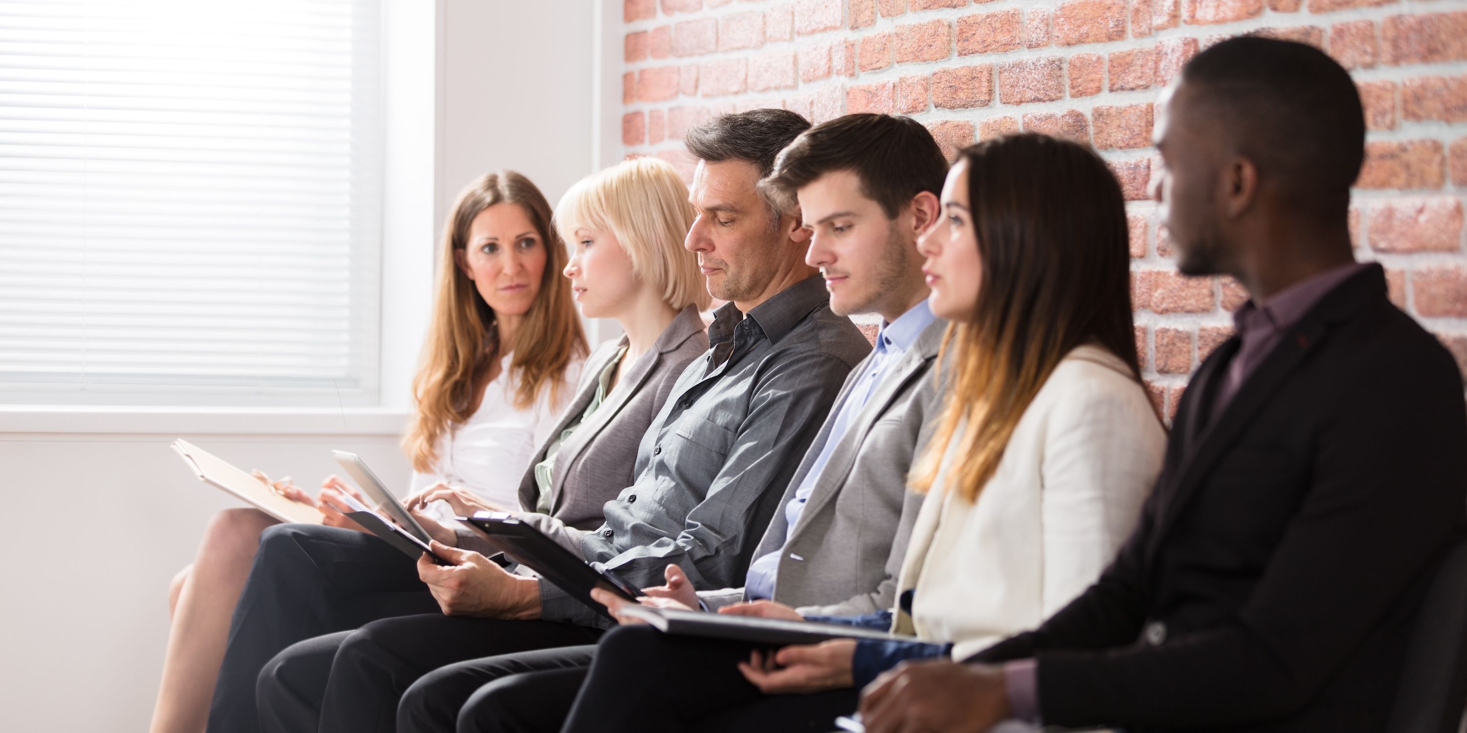 A group of interviewees line up against a brick wall.