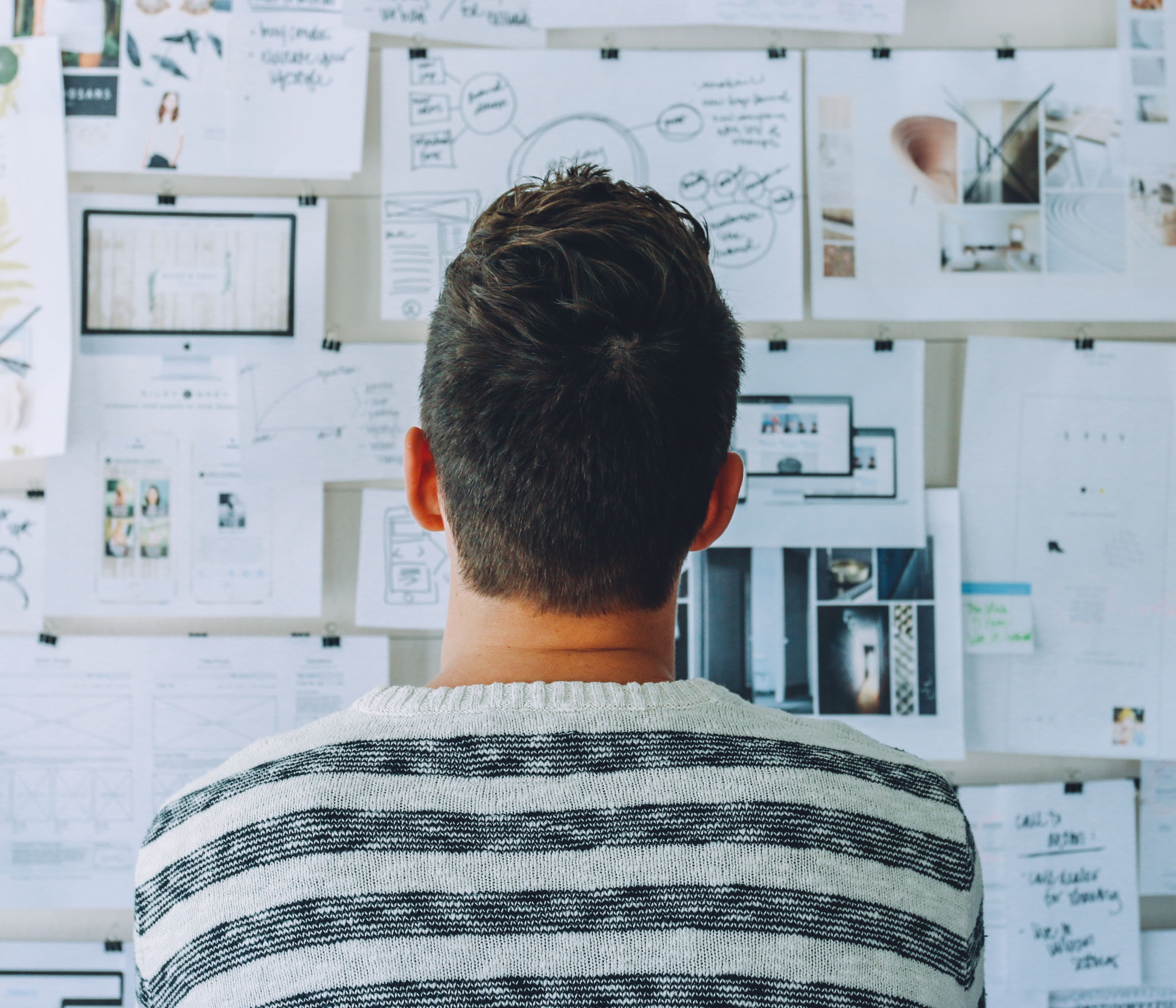 A young person in a striped sweater brainstorms at a wall covered in papers.