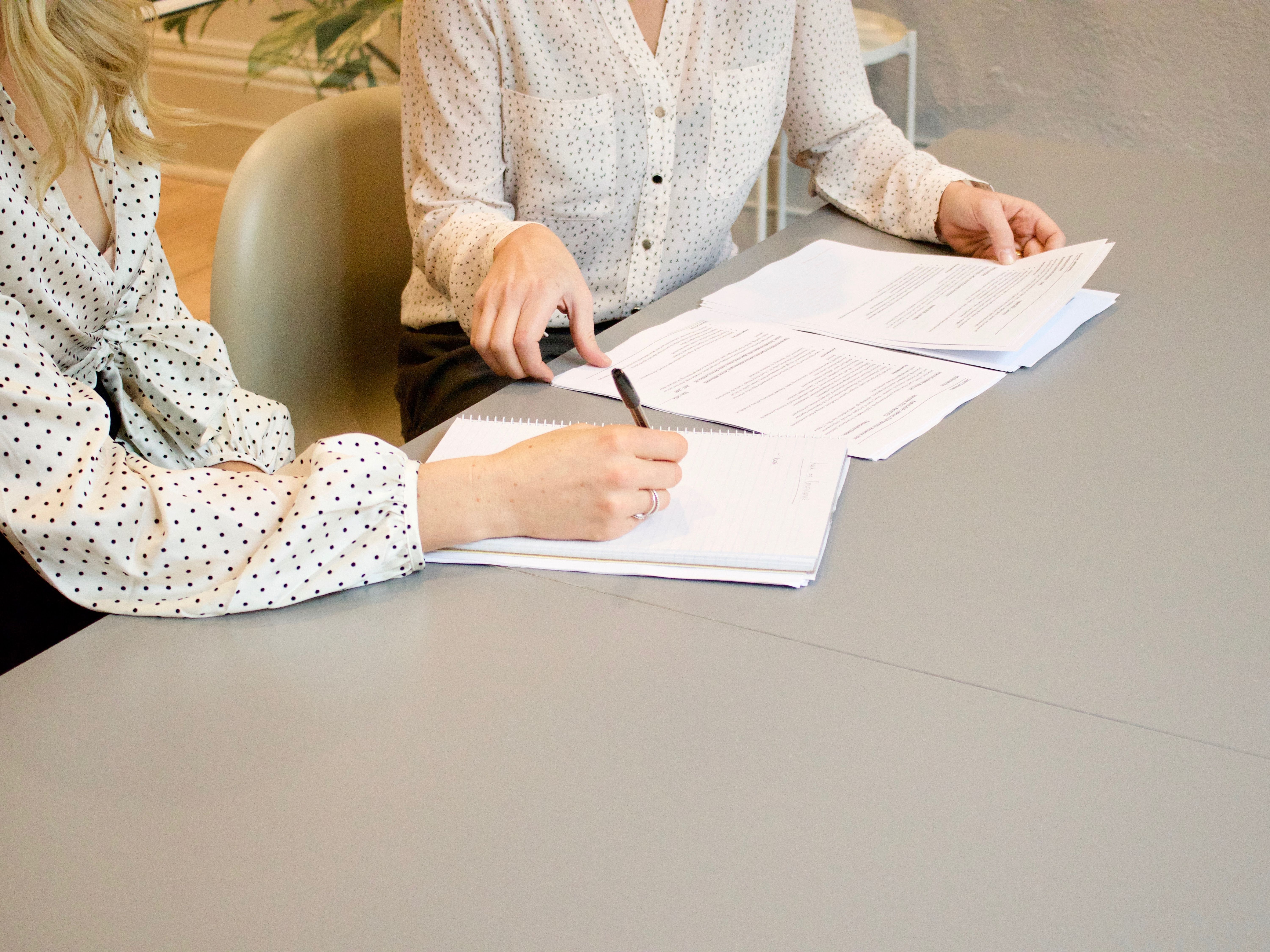 Two women discuss financial consulting at a grey desk.