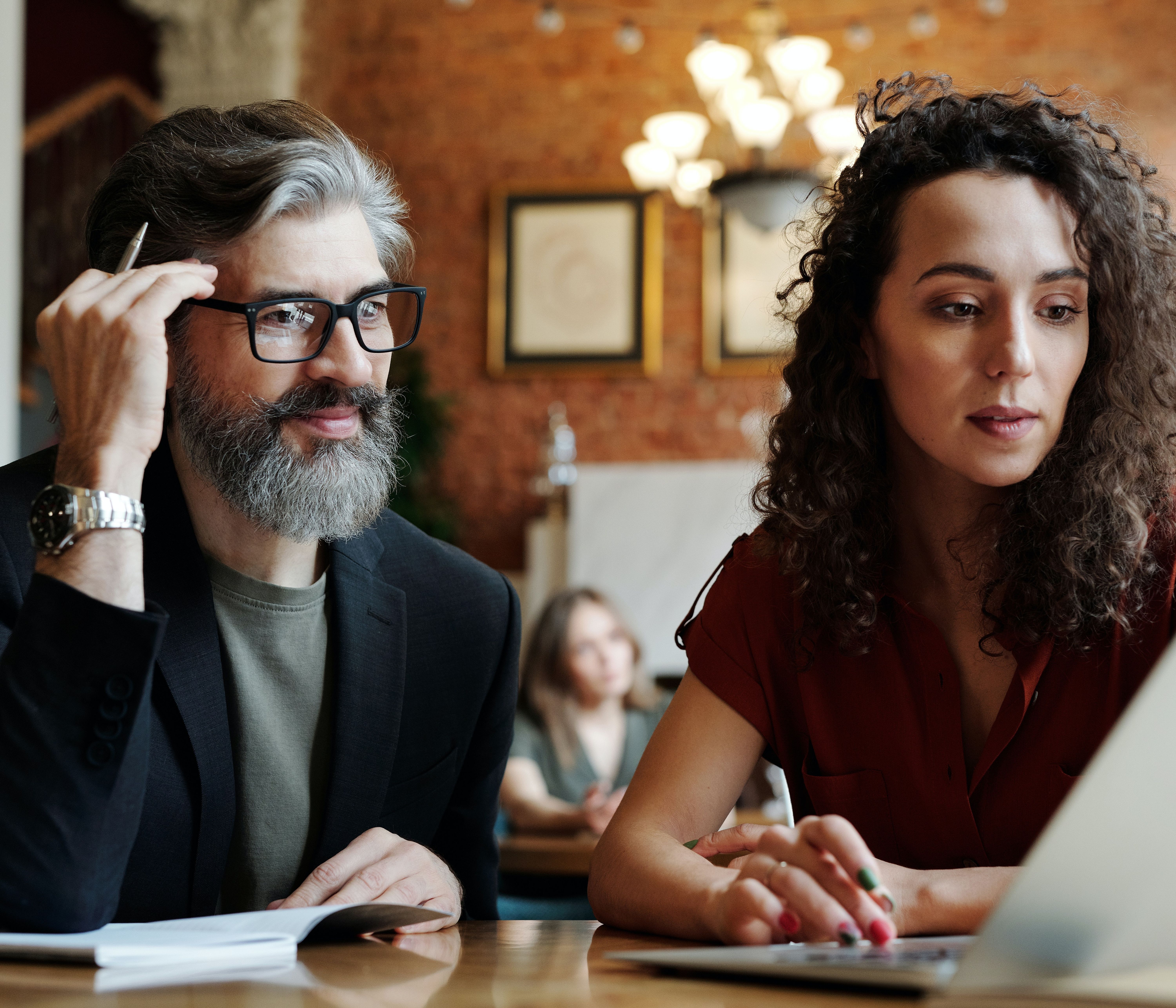 Two trendy middle-aged people work together on financial advising at a cafe.