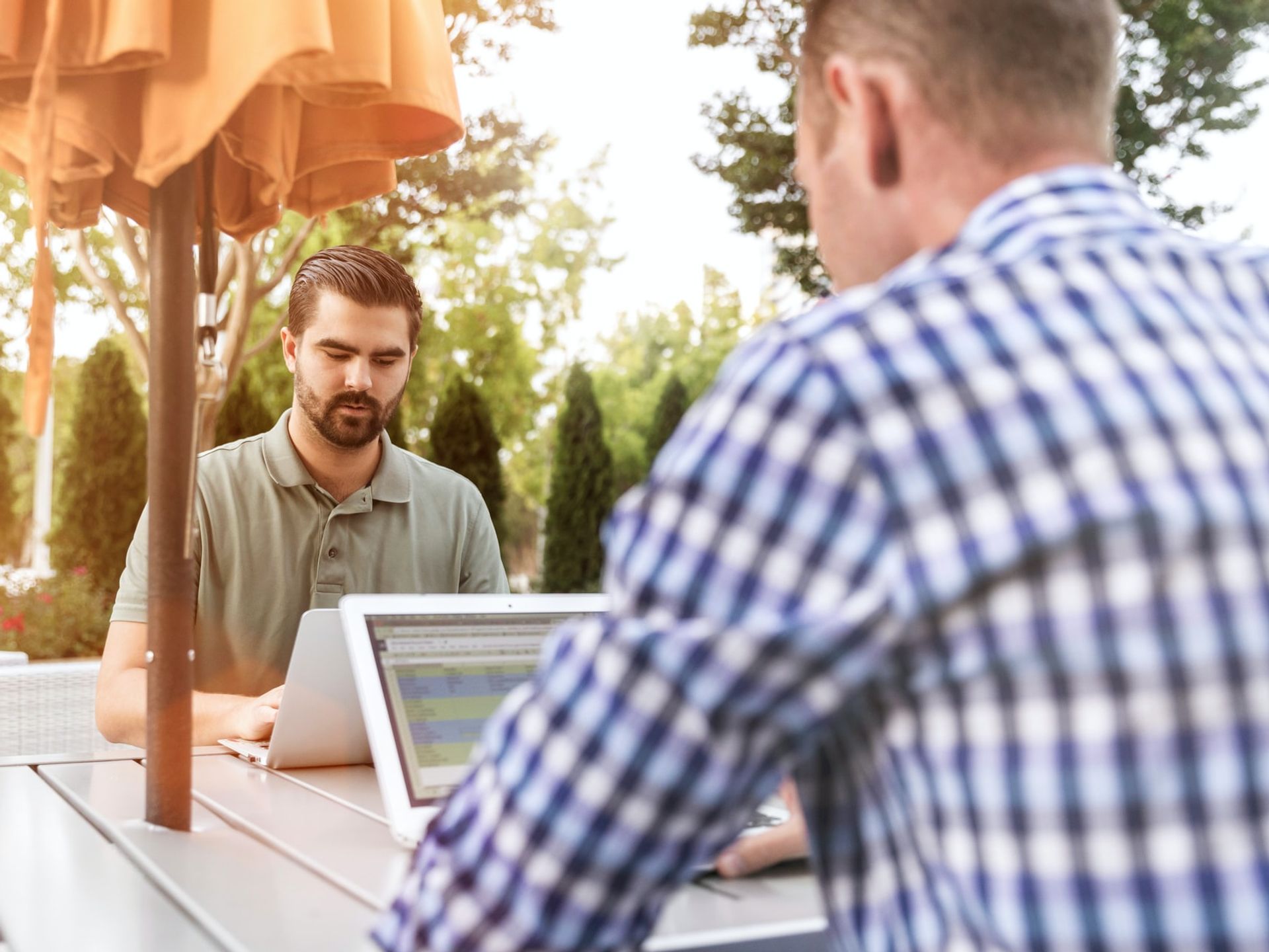 Two business professionals on laptops meet outside at a table with an umbrella to work on LinkedIn Sales Solutions