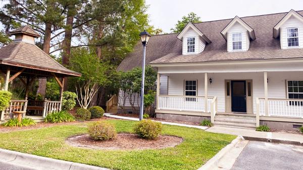 A cute two story office with porch on right with lamppost in front and a gazebo on left with pine trees in the background