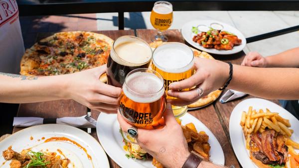 Overhead of three friends touching beer glasses over a table with many different plates of food.