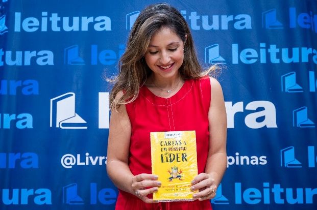 Gabriela Arná sorrindo e segurando o livro Cartas a um péssimo líder em um evento da Livraria Leitura.