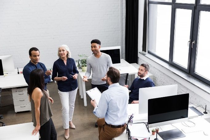 Equipe reunida em um escritório, com uma mulher ao centro conversando com colegas.