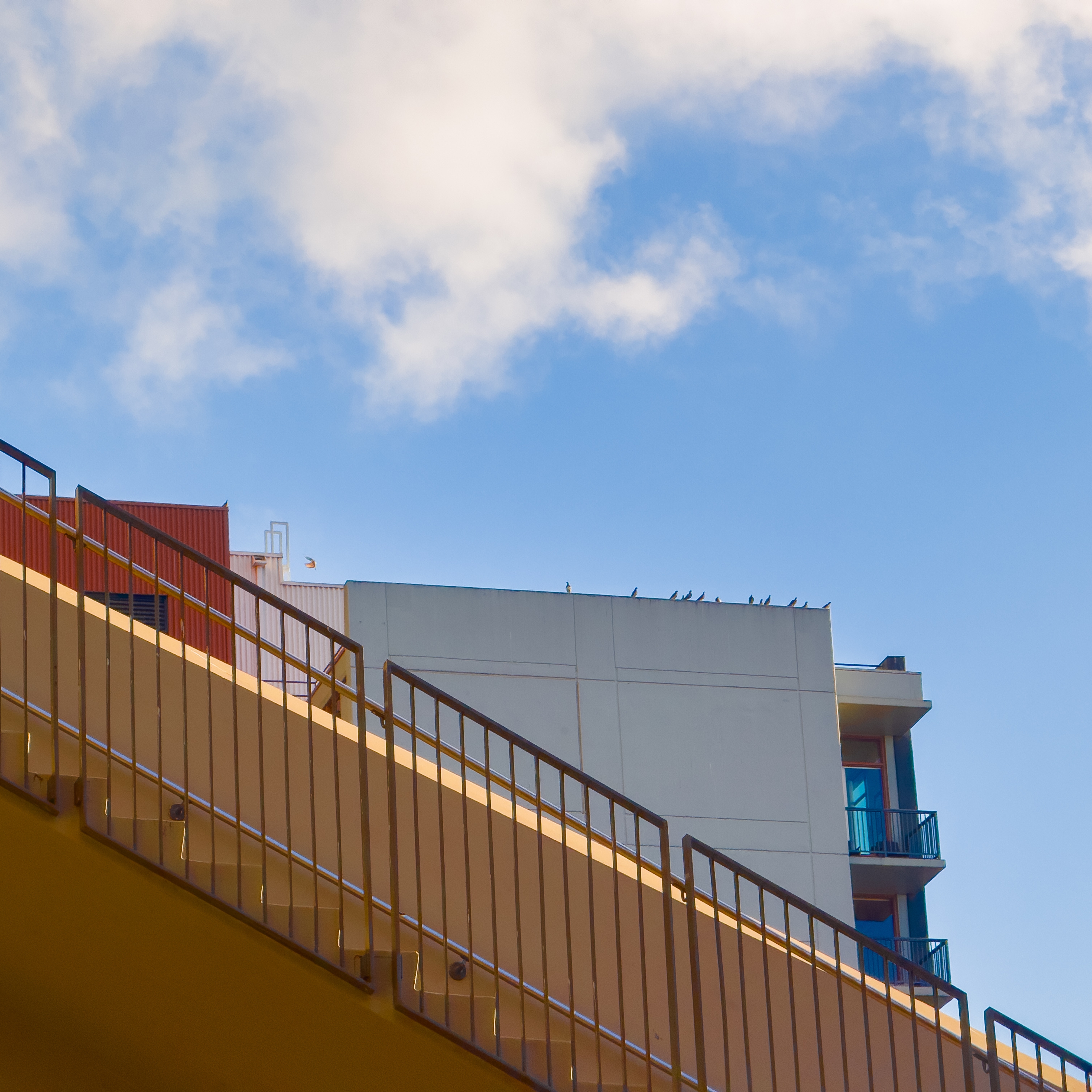 A red building and a light blue building with a yellow staircase cutting sideways in front of them