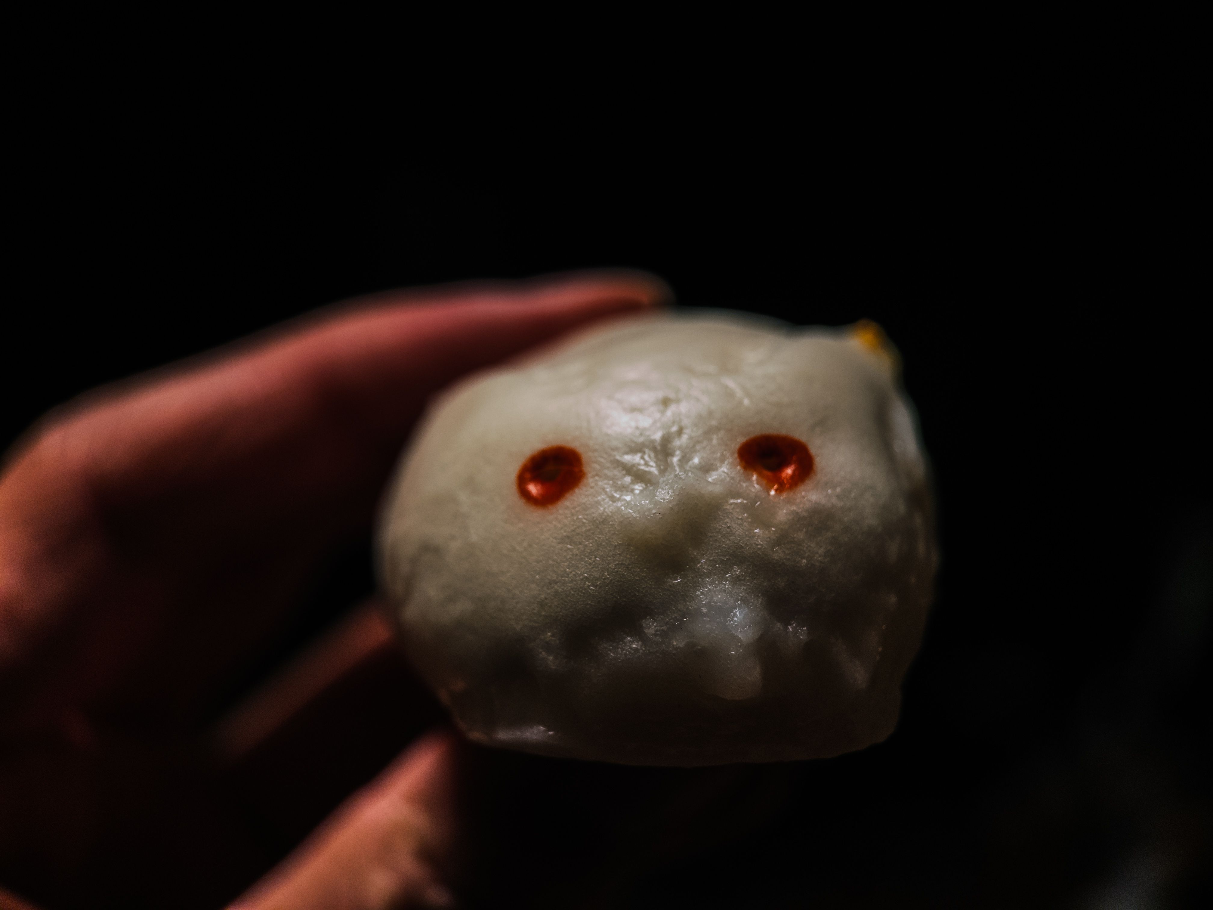 A hand holding a bunny-shaped custard bun (bao) facing the camera with red eyes