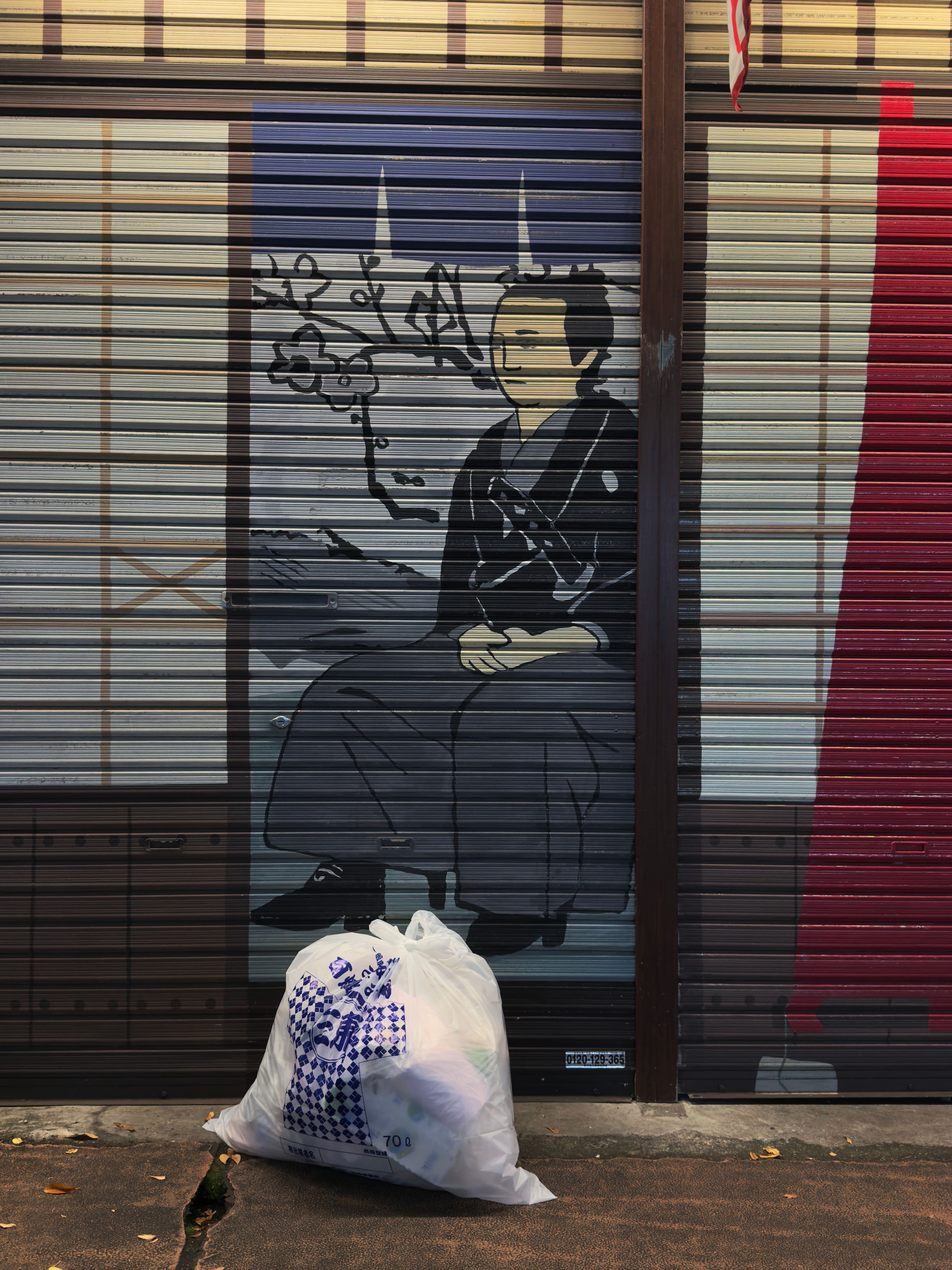 A mural on a garage-style door of a man sitting down. In front of the door is a trash bag full of trash.