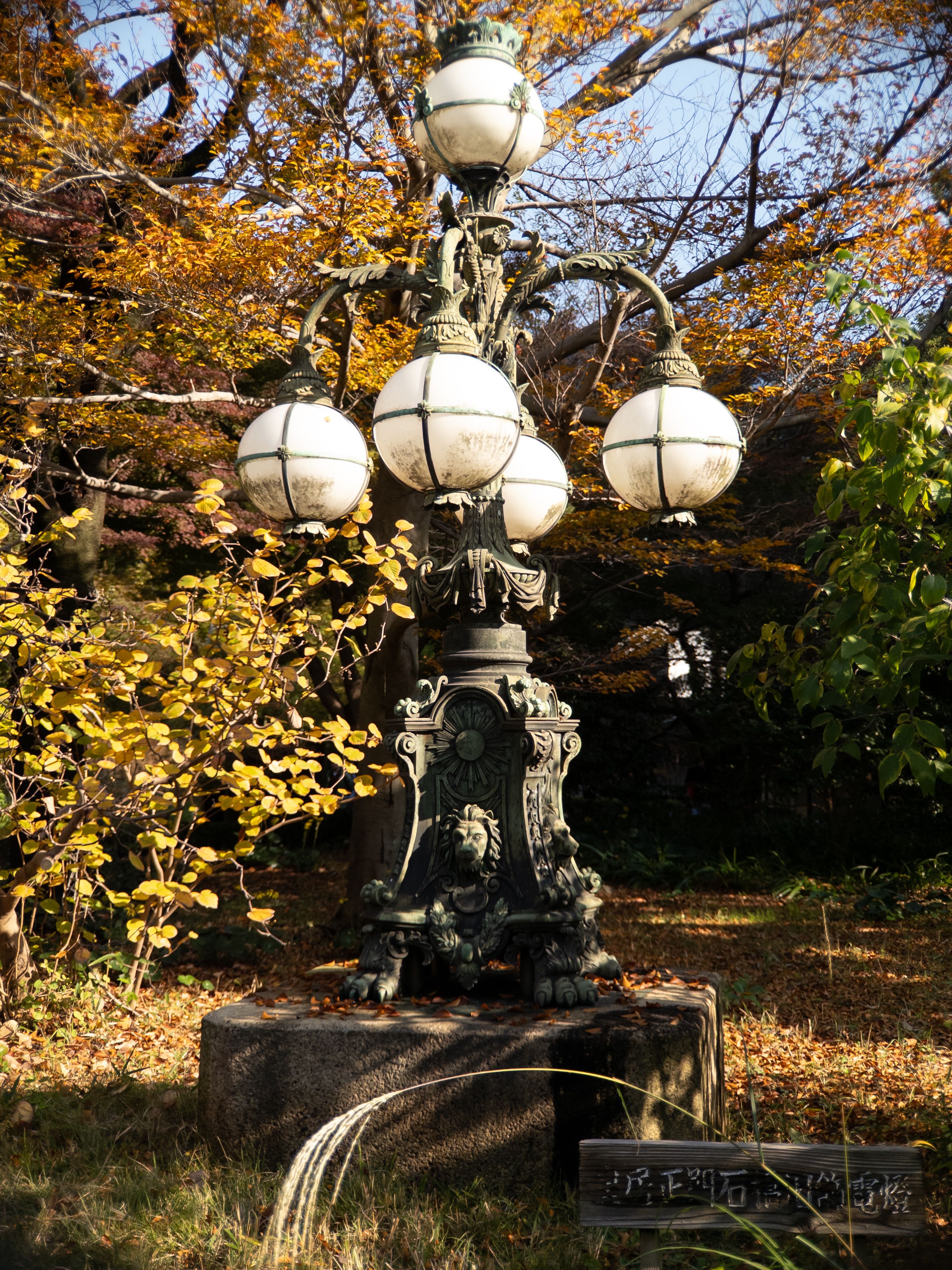 A short, ornate street light with four light globes hanging around the pole and one light globe at the top