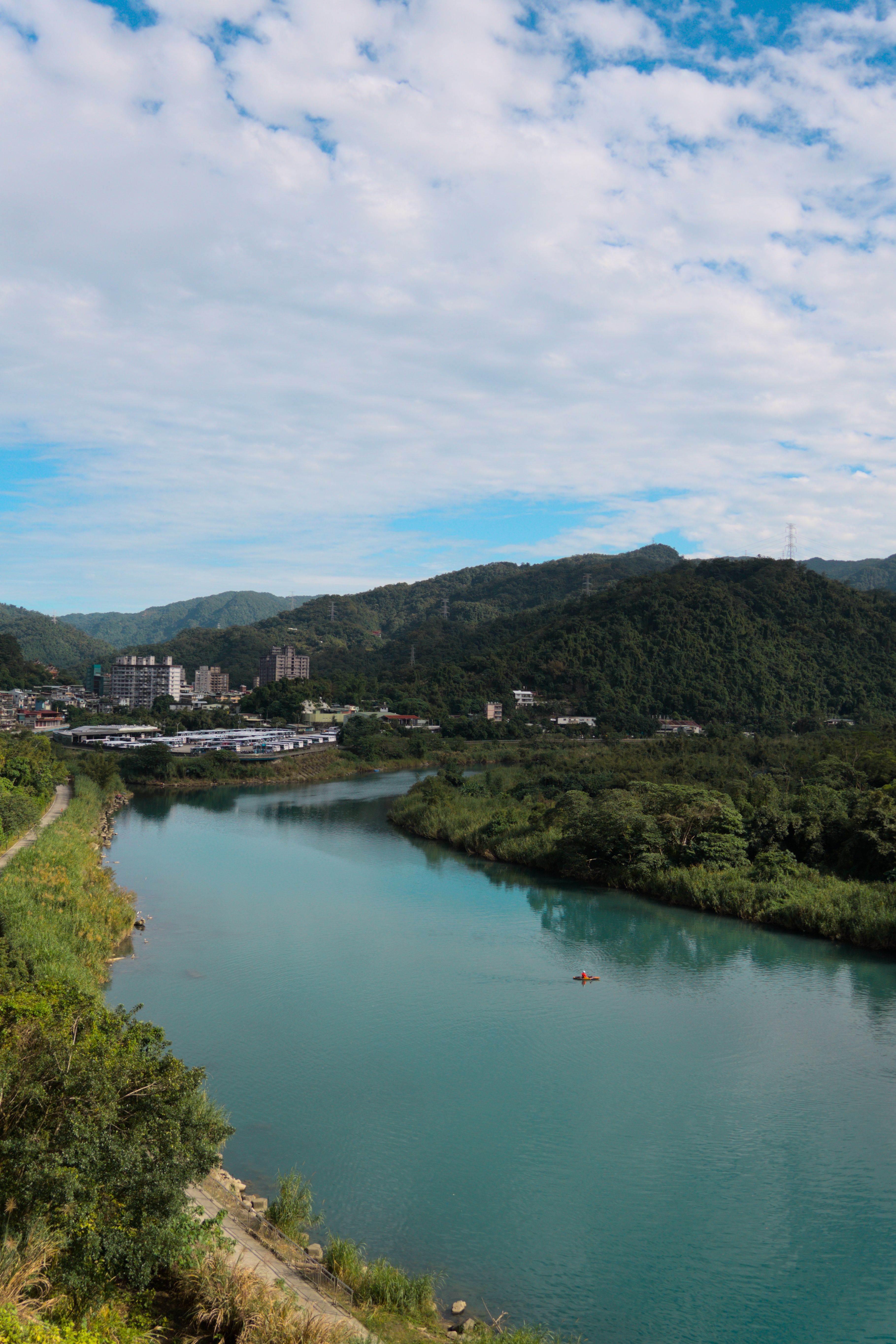 A kayaker in an orange kayak wearing all orange kayaking down a wide, calm, turquoise river through forested hills.