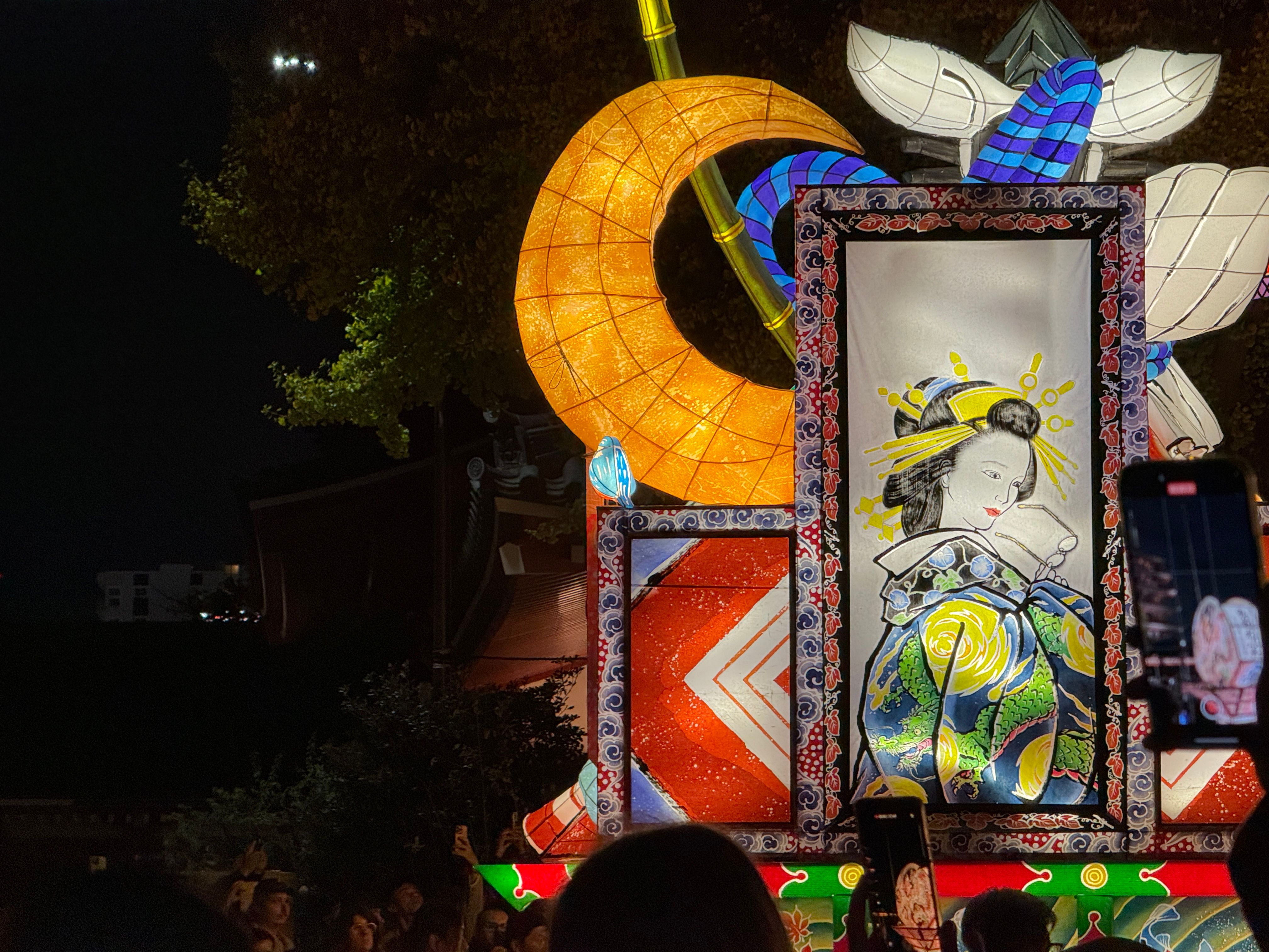 A wire and paper lantern style light up parade float at night showing a woman holding a pair of glasses.