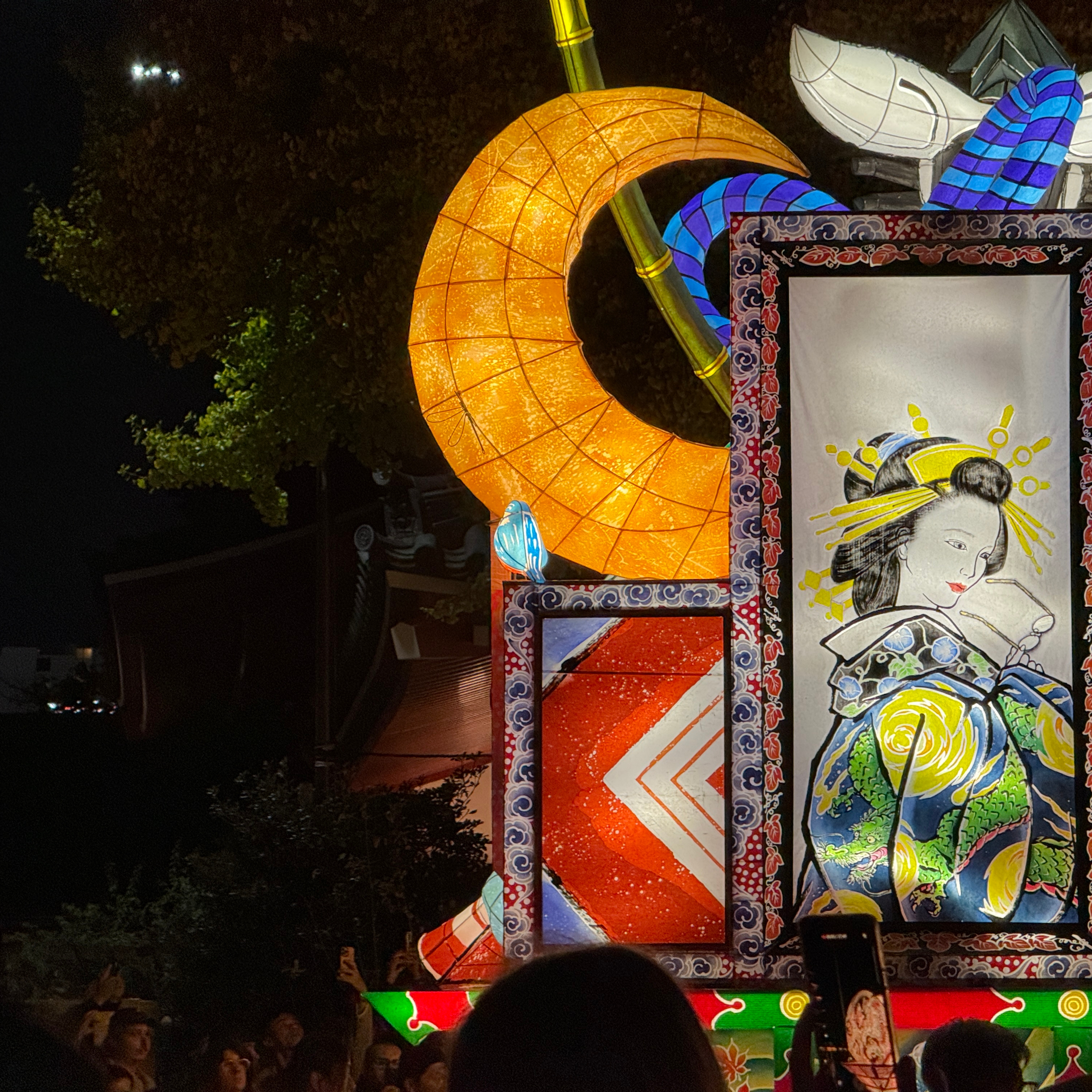 A wire and paper lantern style light up parade float at night showing a woman holding a pair of glasses.