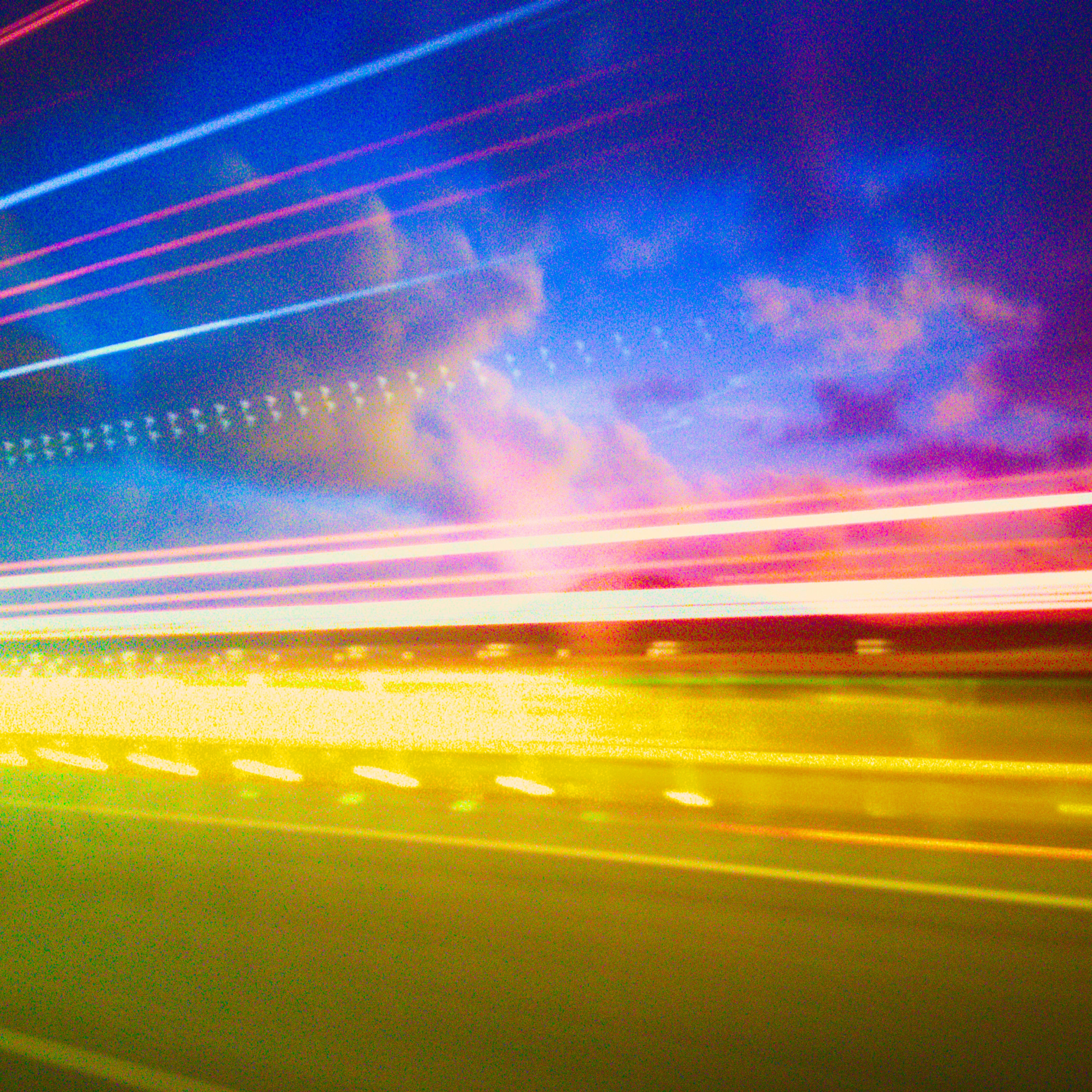 A long exposure photo at dusk of clouds behind a truck driving past. The truck is only visible as streaks of light.