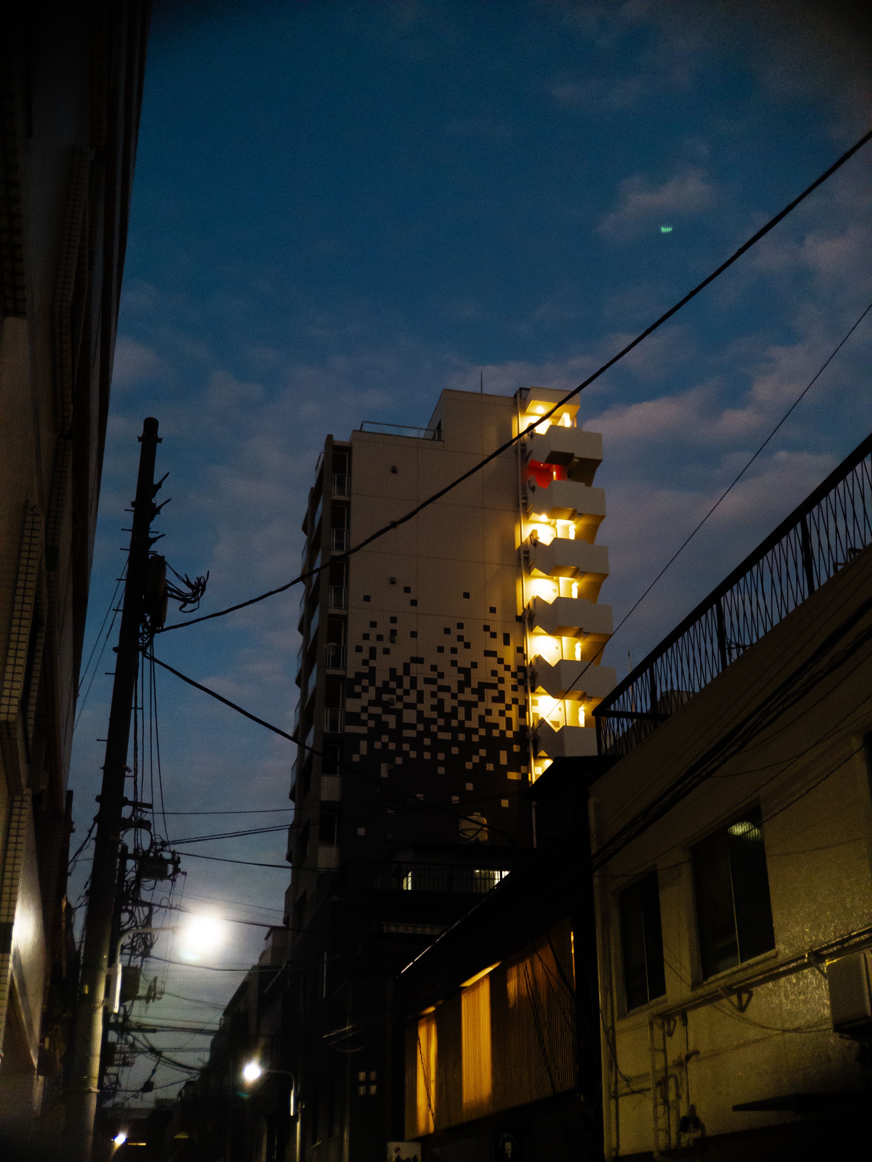 An apartment building at night with a lit up external stairway. The second from the top floor has a red light instead of a white one.