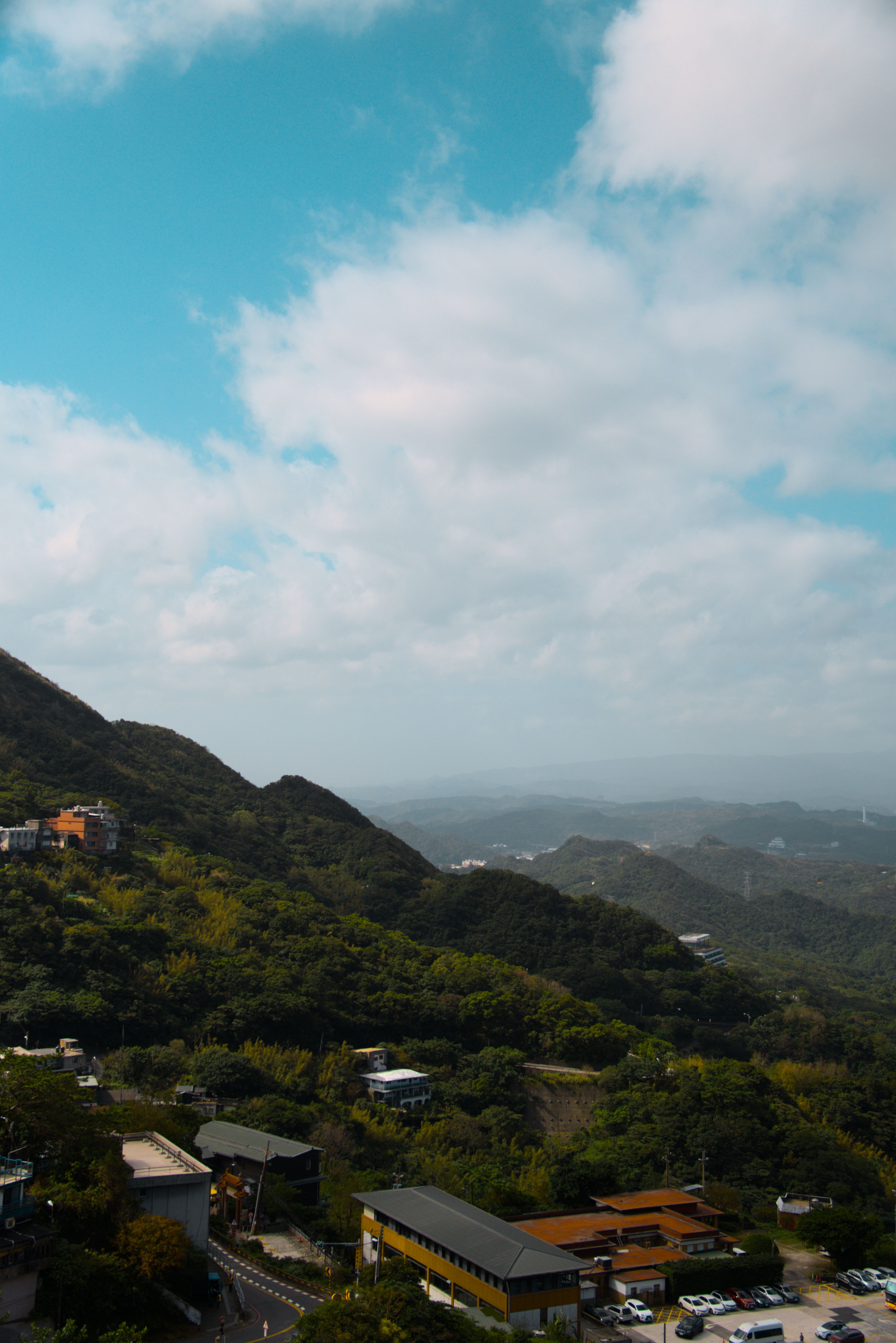 A forested hillside with a few buildings at the bottom. More hills stretch off into the distance.