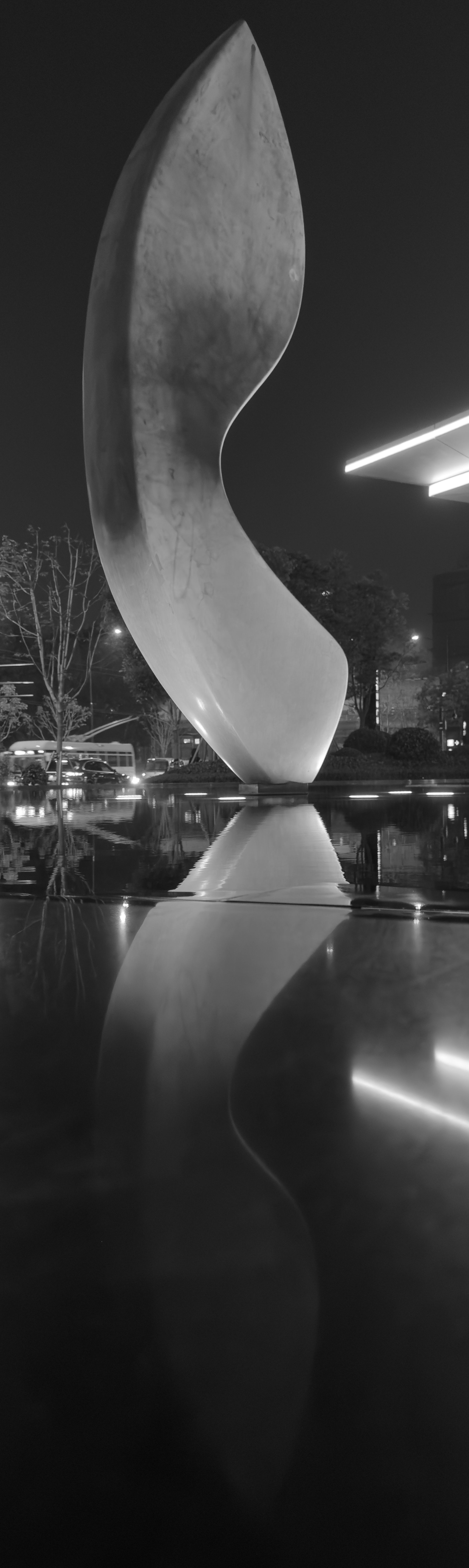 A black and white picture of a sculpture that looks like a giant stone knife, standing blade up in a small reflecting pool