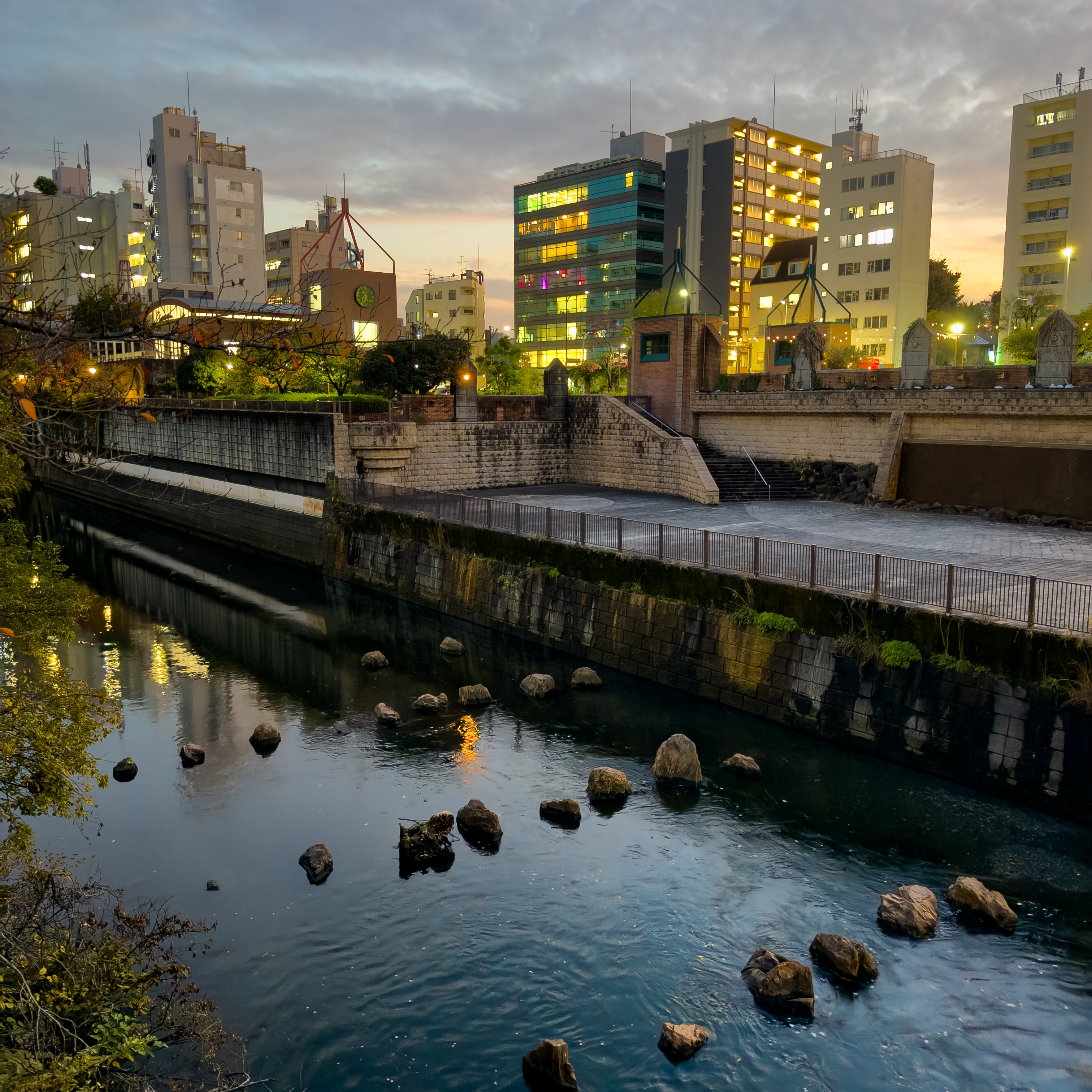 A canal through Tokyo at sunset, with lines of rocks laid across the canal as if for stepping stones