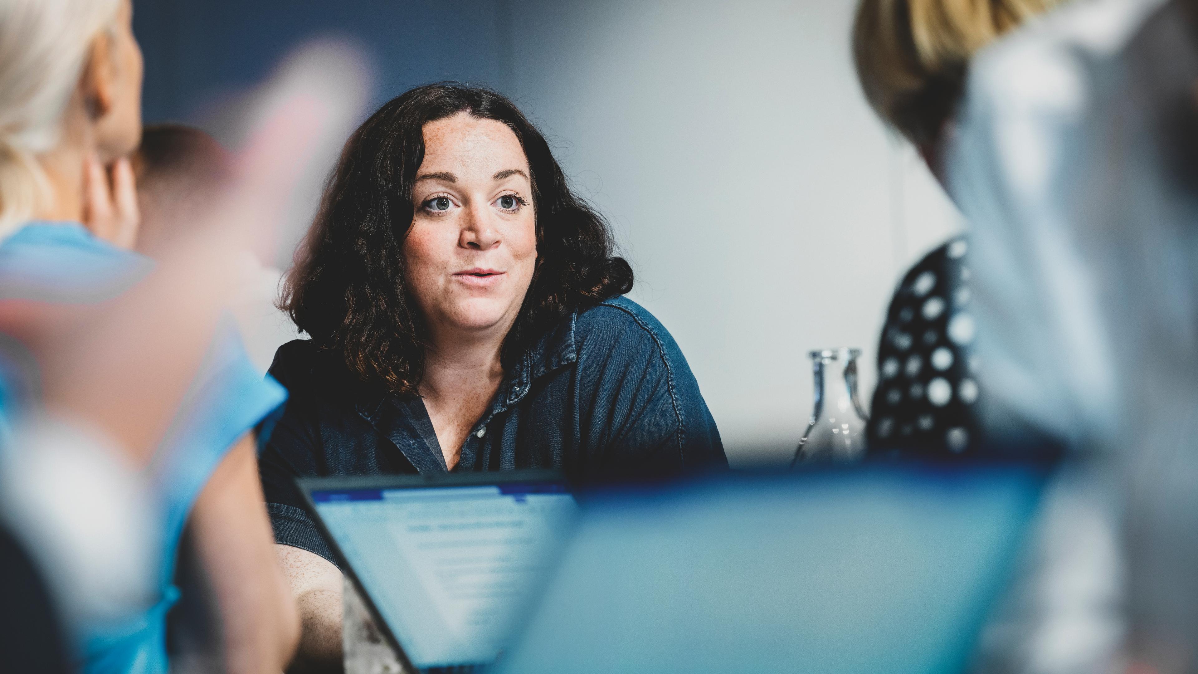 3 woman sitting at a conference table discussing, listening