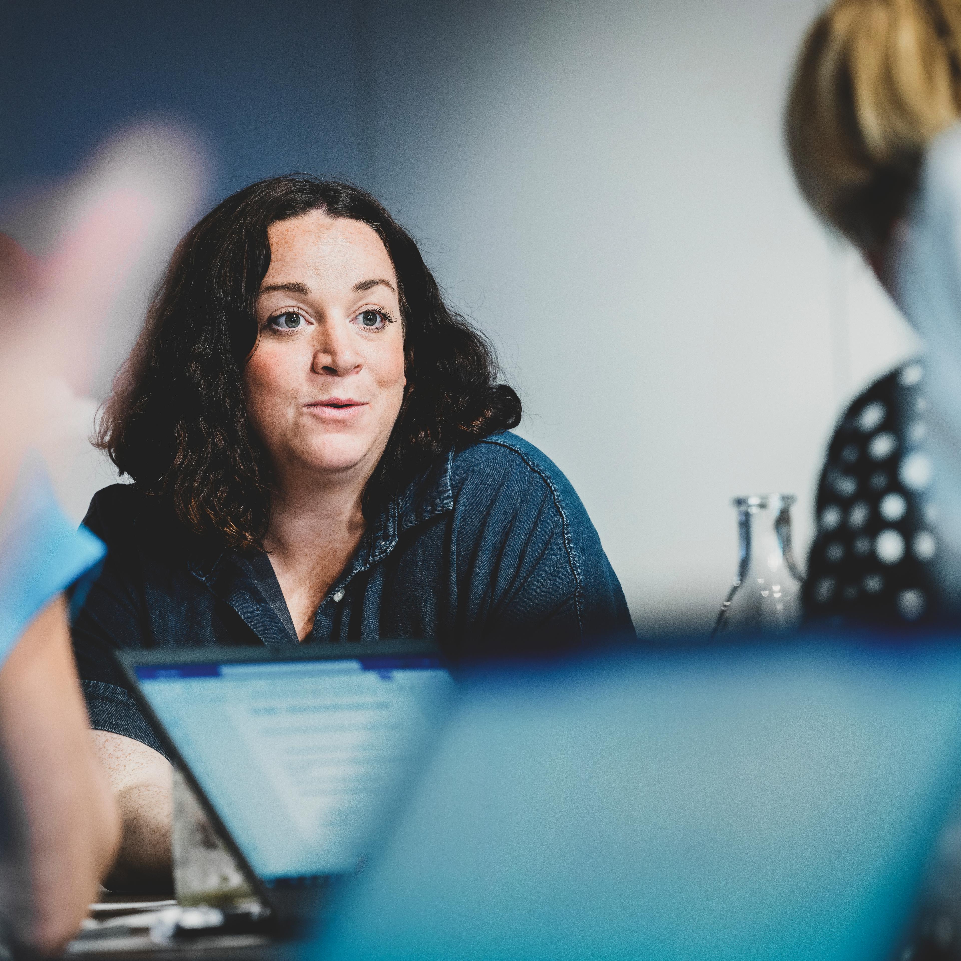 3 woman sitting at a conference table discussing, listening