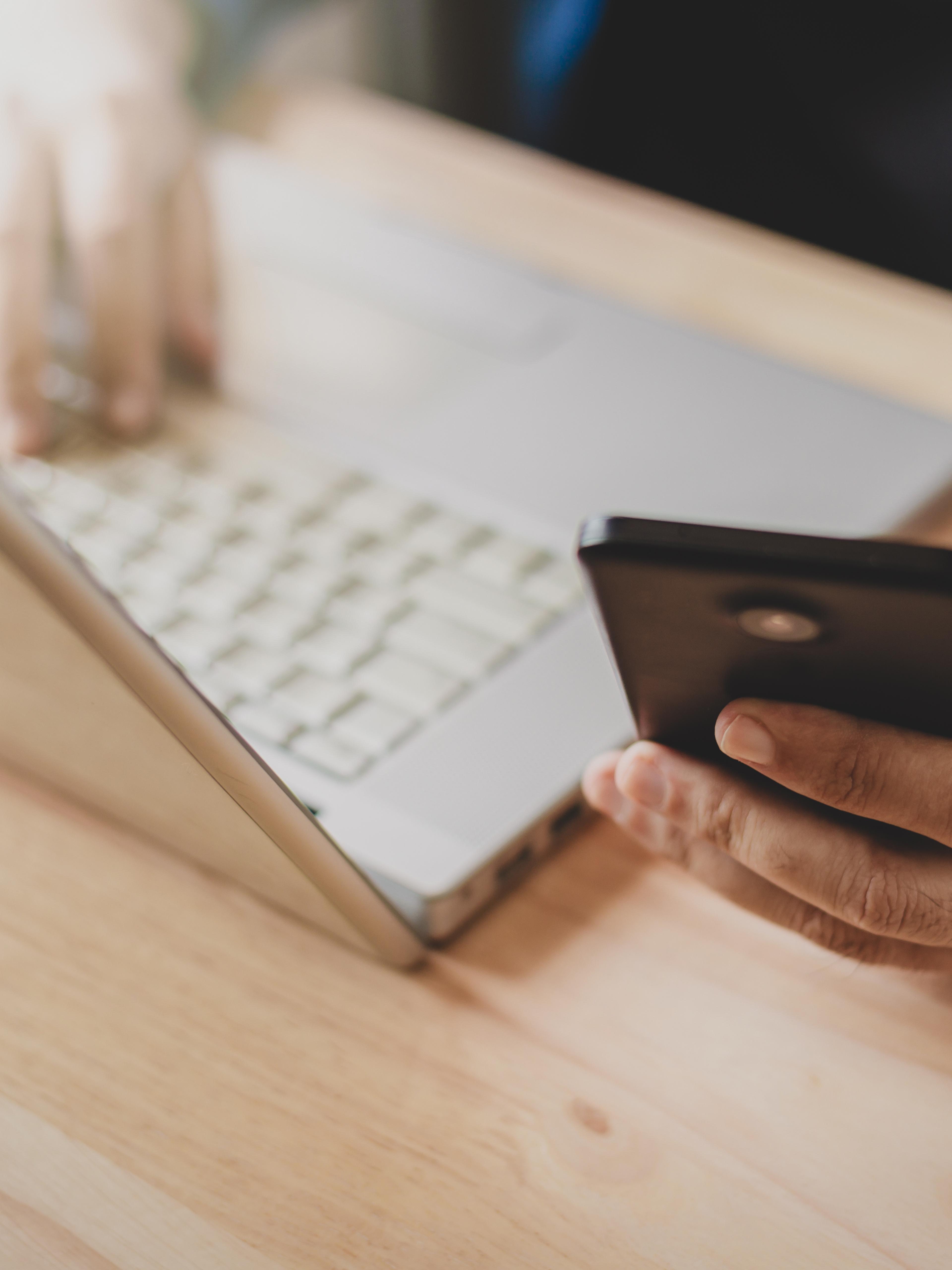 A desk with laptop and a person holding a phone
