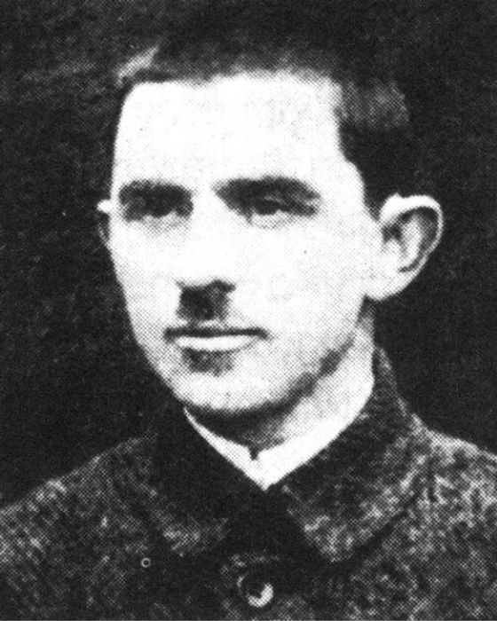 Photograph of man in dark button shirt with a small moustache.