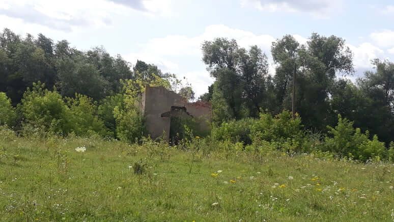 Photograph of a green field with ruins of a single building in the background.