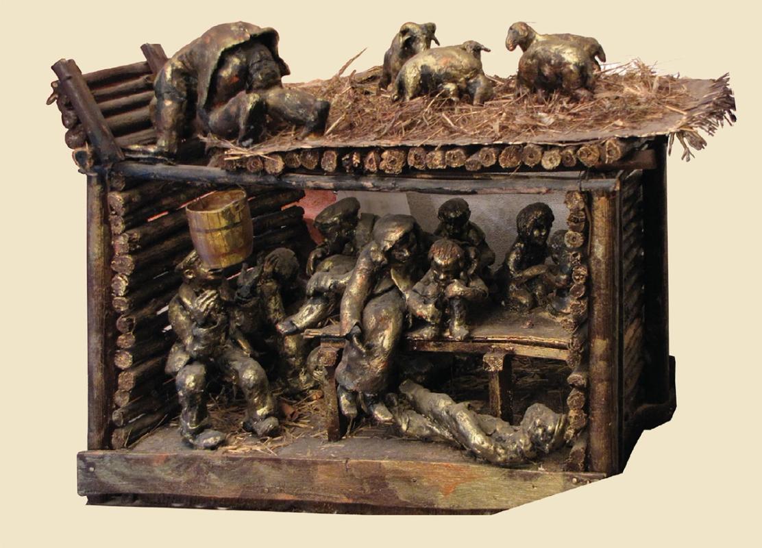 Small sculpture of a group of people crowded into a hiding place under a barn. A man is bringing water to them.