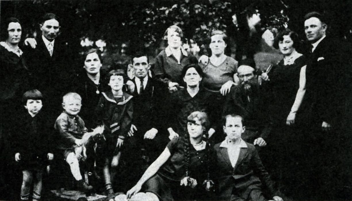 Photograph of a large family with several men, women, and children all in darker clothing in 1930s-era clothing.