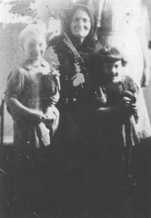 Older woman in dark clothing standing with two young girls.