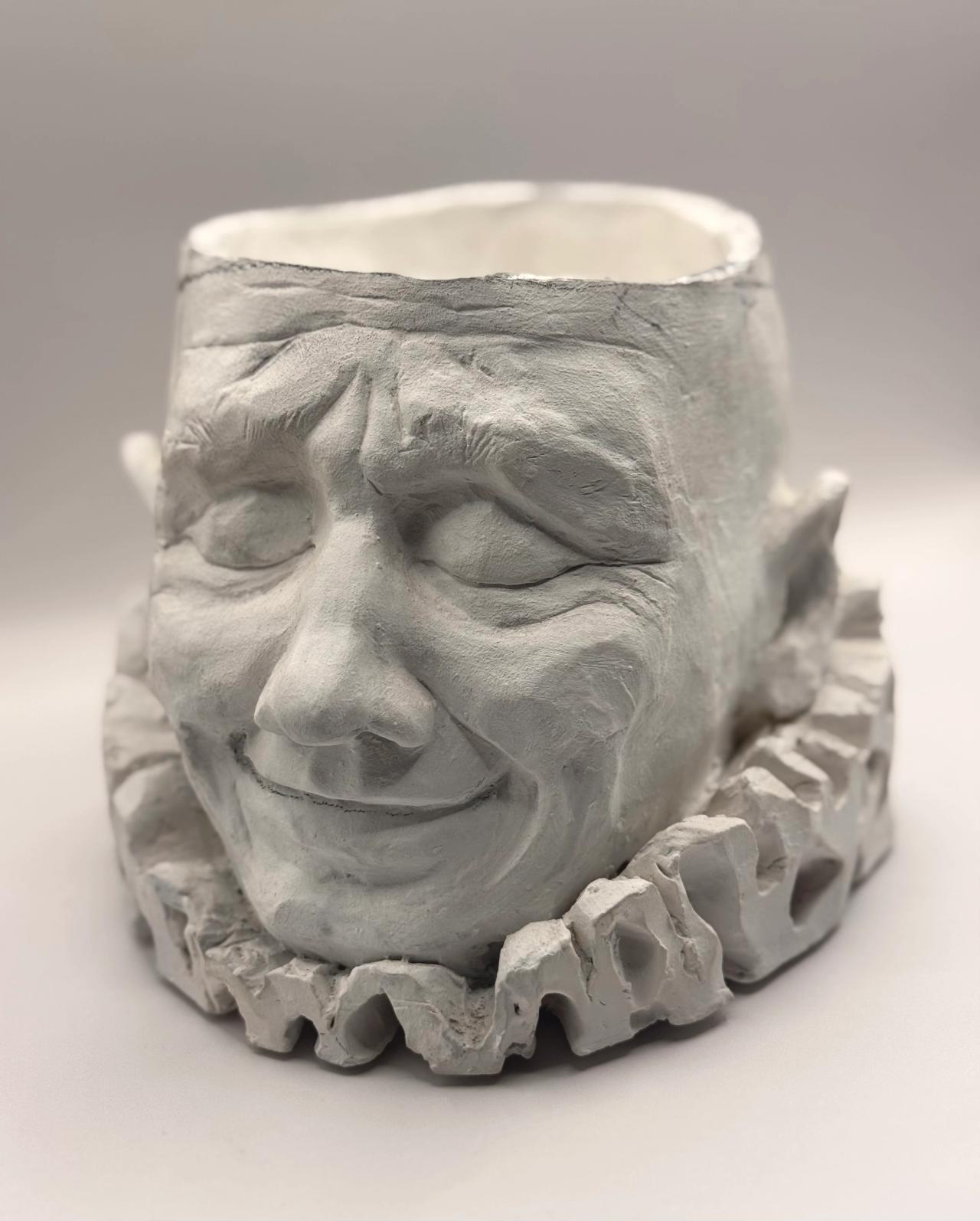 The smiling clay face seen from above at an angle, showing its hollow top and ruffled collar