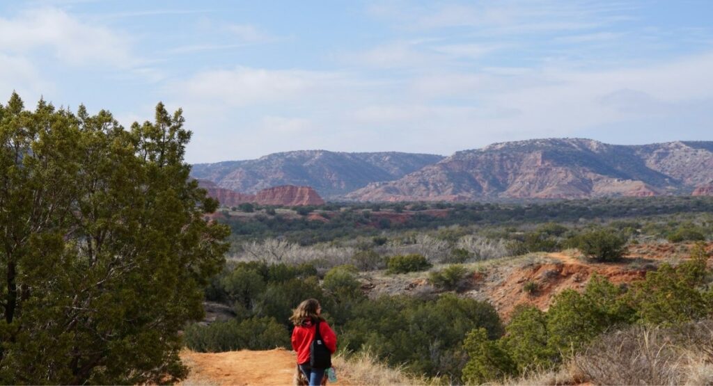 A hiker in a red jacket takes in the sweeping views of Palo Duro Canyon's rugged red rock formations