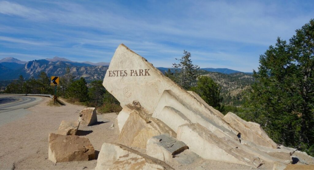 "Estes Park" engraved on a large natural stone monument beside a winding mountain highway
